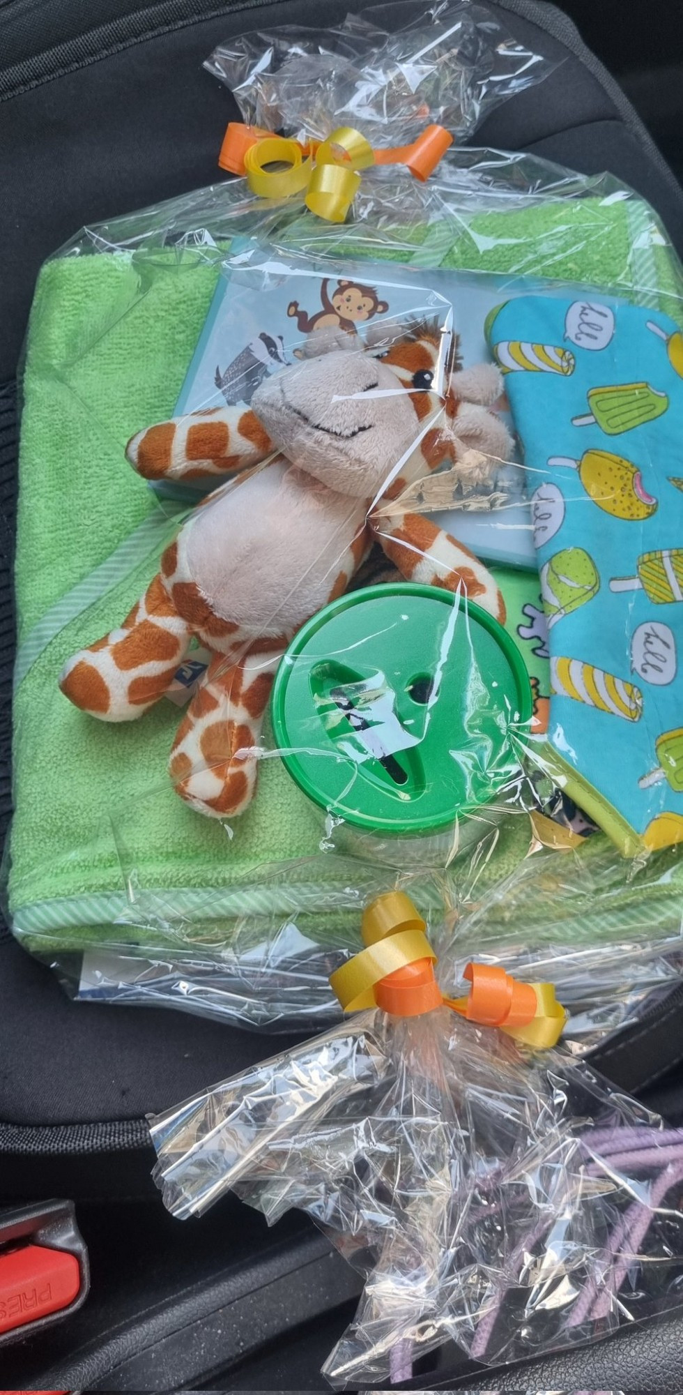 Durchsichtiges Geschenkpapier, eine kleine Plüschgiraffe, ein Lätzchen mit Stieleis darauf, ein kleines Buch mit Dschungeltiere und ein grünes Handtuch