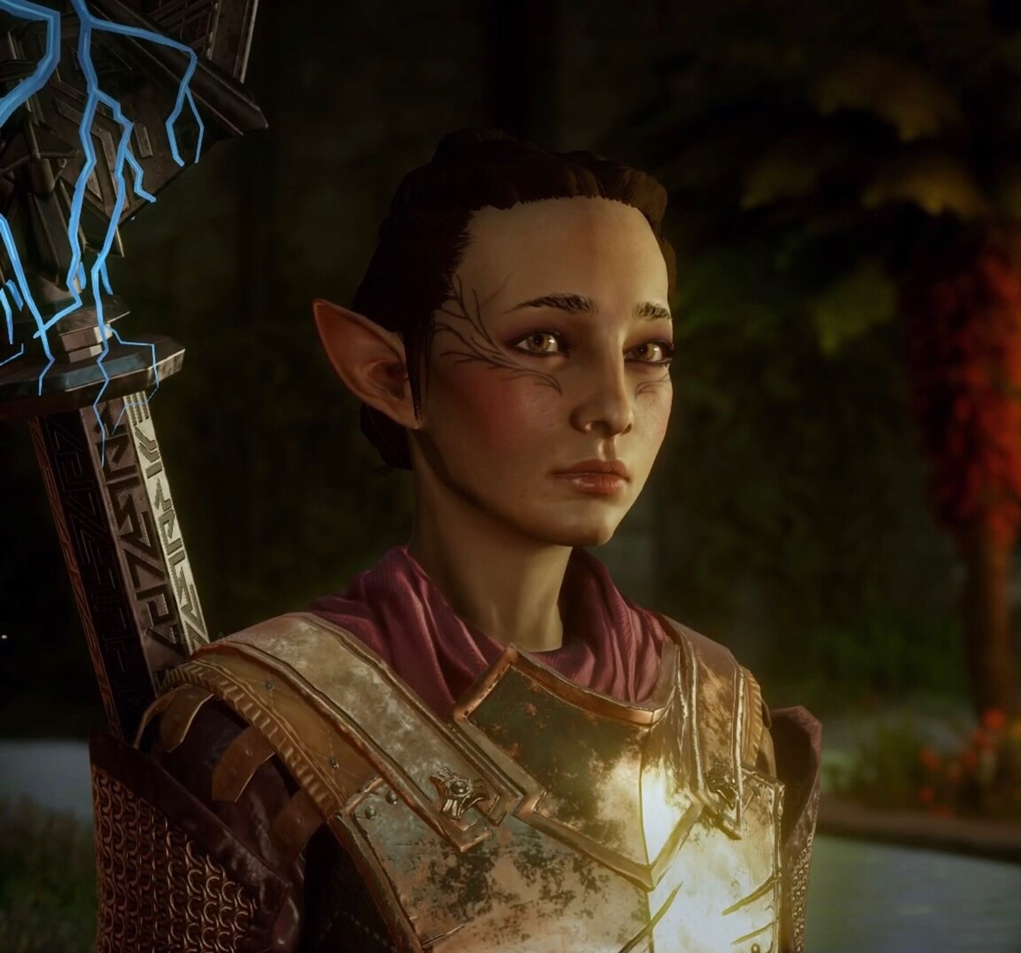 Inquisitor Valylle Lavellan as she appears in game. She has the braided up bun hairstyle, dark brown hair, hazel eyes, and Mythal’s simplified vallaslin (face tattoo). She’s wearing a maroon scarf with a gold chest plate, and chainmail and leather pauldrons. She has the lyrium imbued staff on her back from the Descent DLC