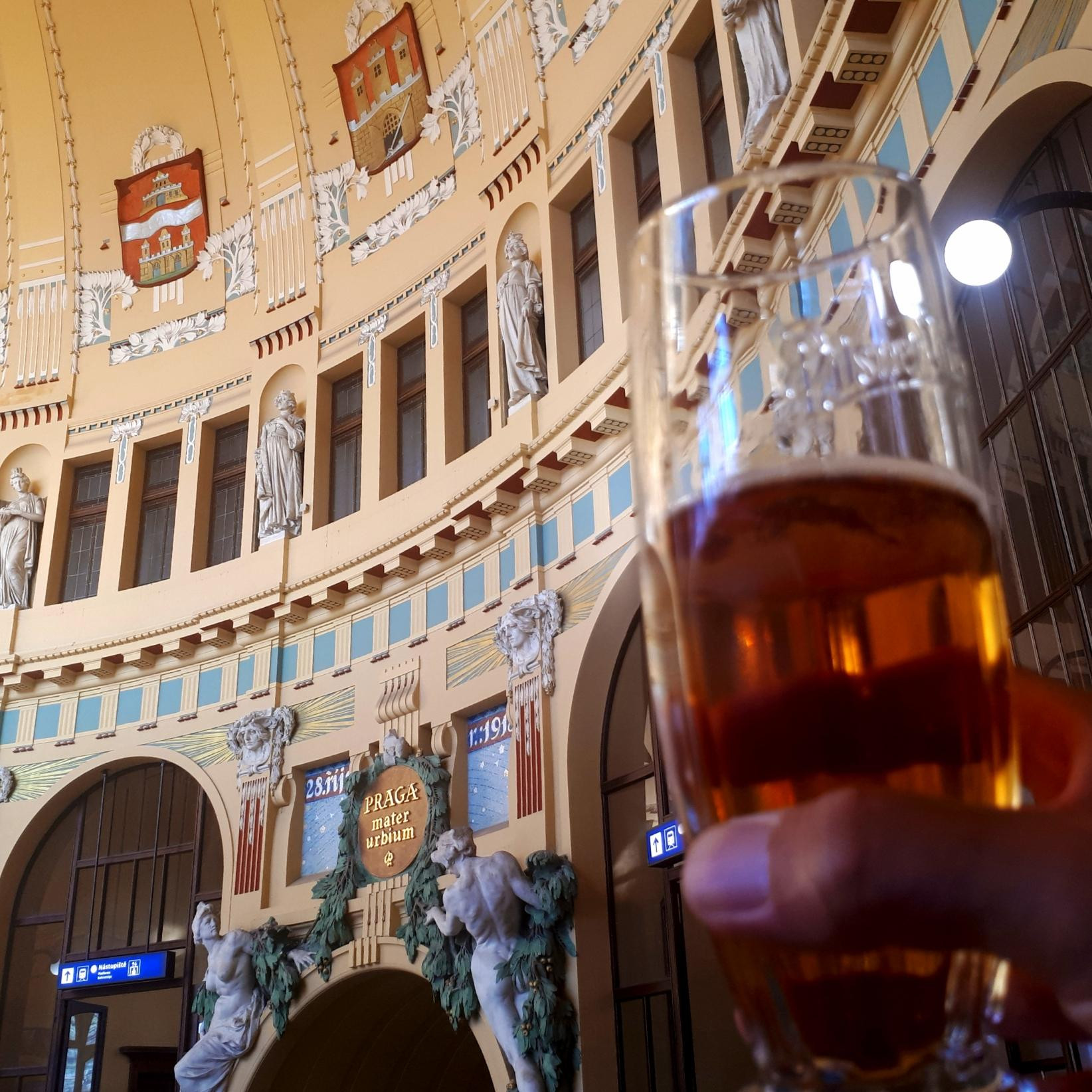 A glass of beer and part of the ornate old part of Prague central station.