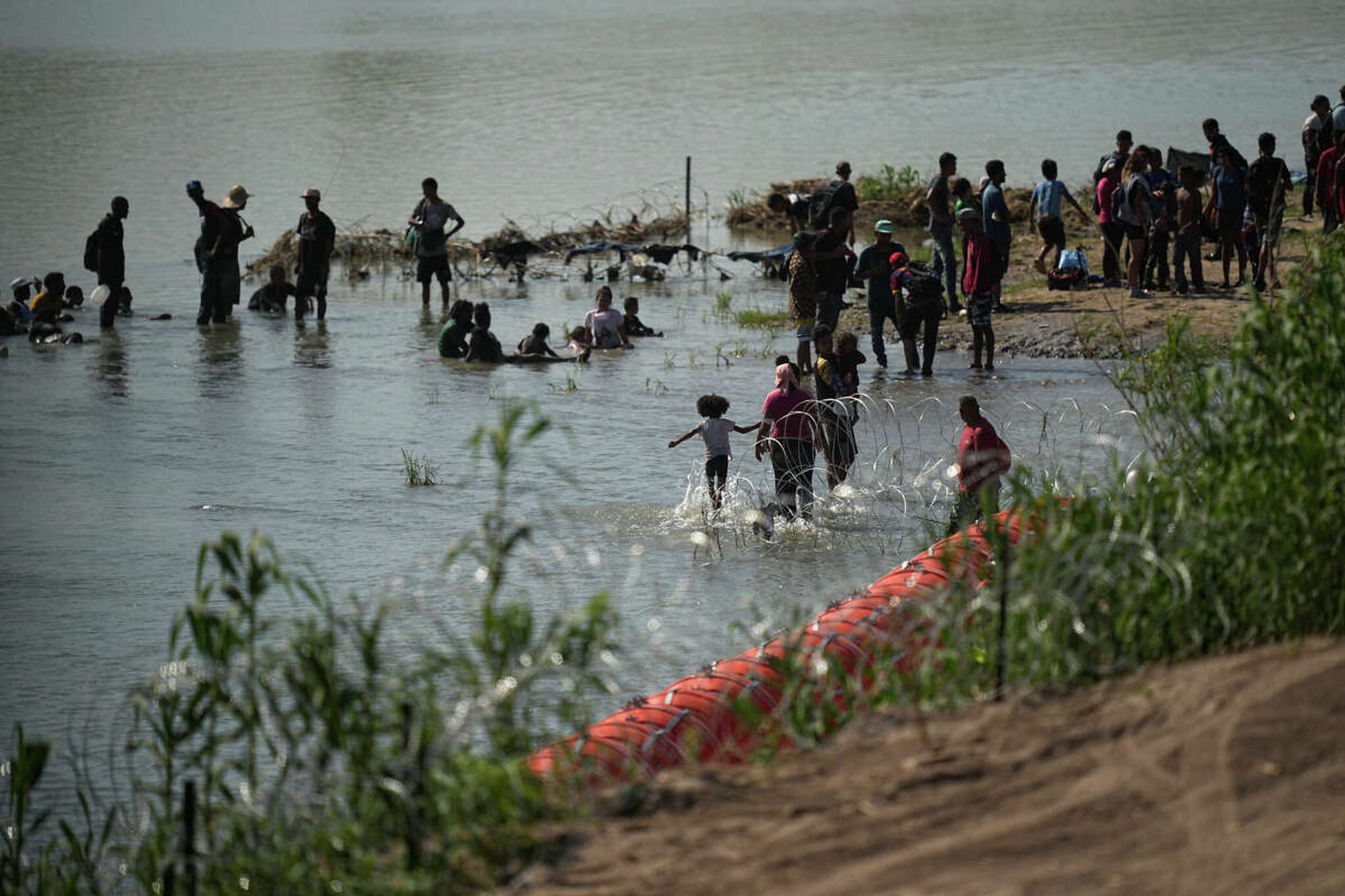 Migrants cool themselves in the waters of the Rio Grande after crossing to the U.S. from Mexico near a site where the state is installing large buoys to be used as a border barrier along the Rio Grande near Eagle Pass, Texas, Monday, July 10, 2023.