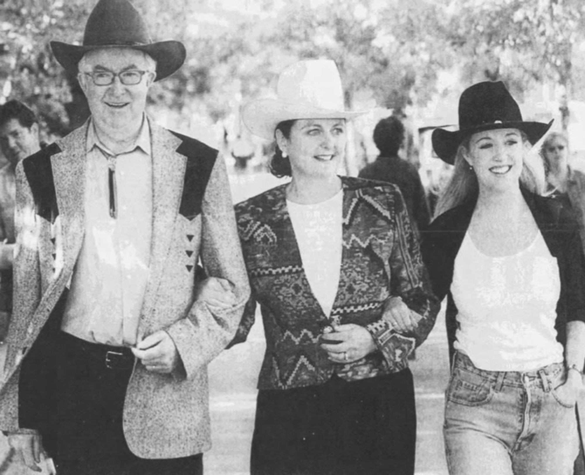 A man in a black hat walking arm in arm with a woman in a white hat, who has a woman in a black hat walking next to her.