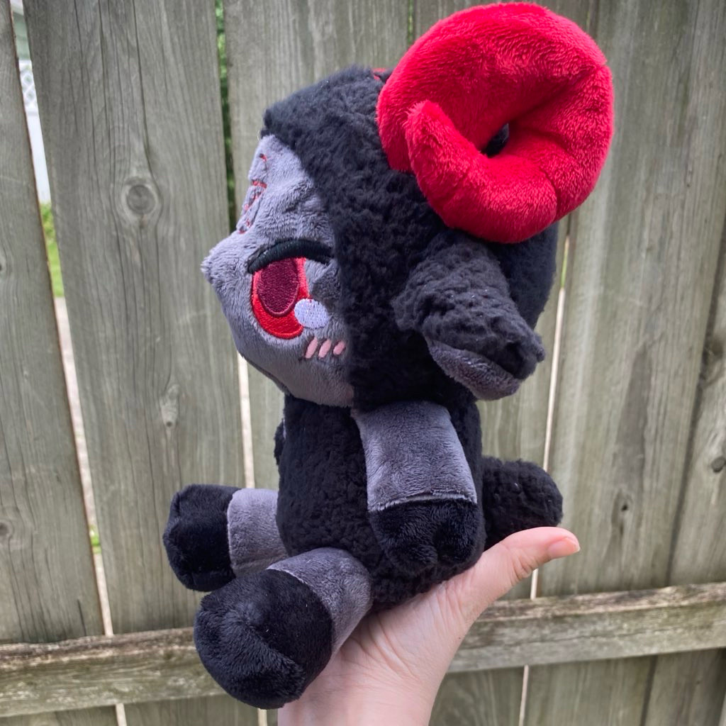 A side view of a black, gray, and red sheep demon plushie