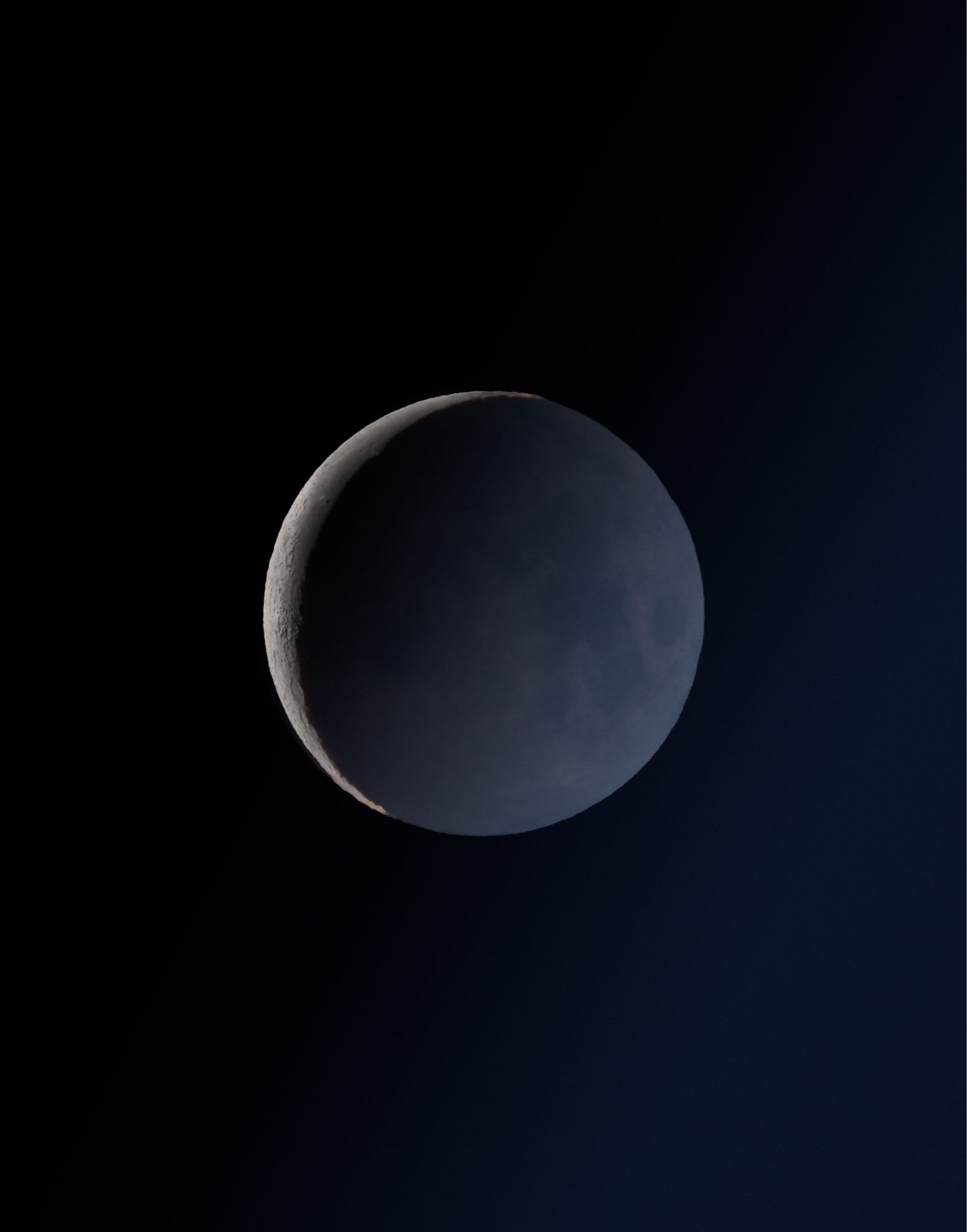 moon mostly in shadow with bright detailed detailed strip of crescent and more muted colors of earthshine