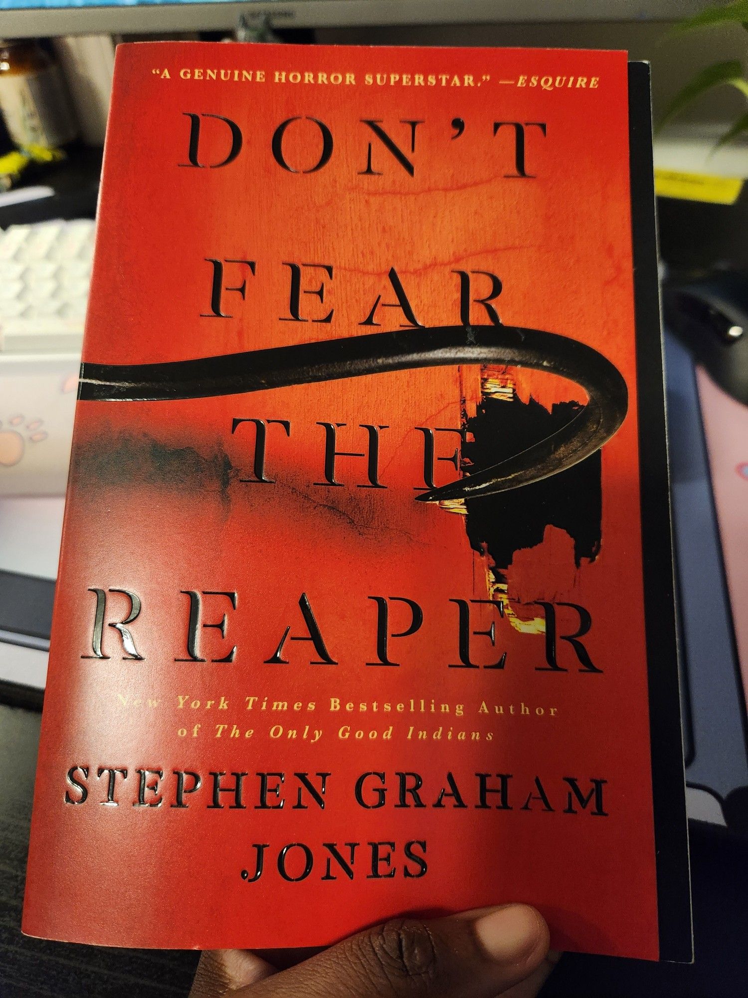 A photo of Stephen Graham Jones' novel, "Don't Fear the Reaper". The book cover is blood red with a crowbar digging a hole through a door.