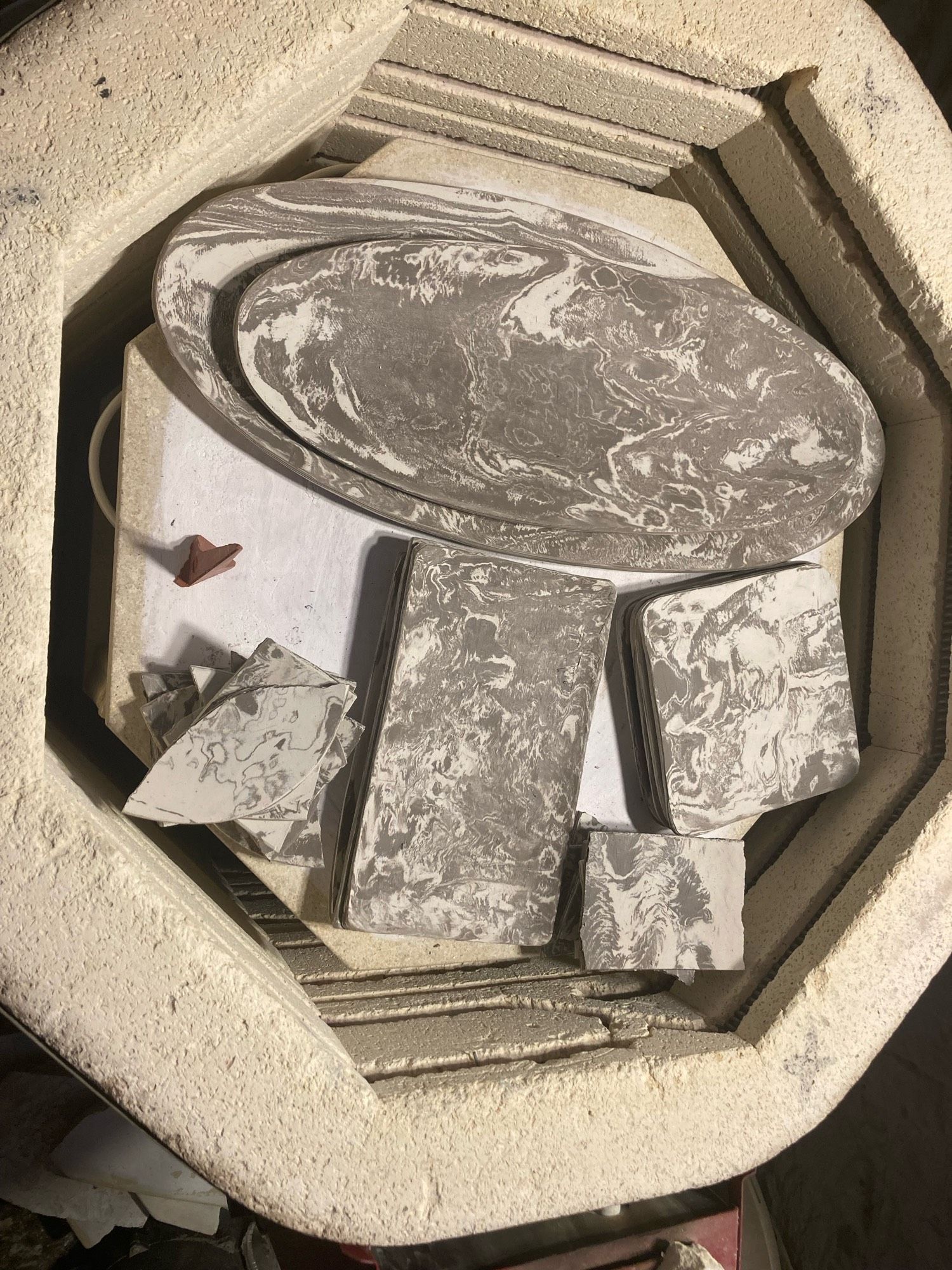 Marbleized plates and shards stacked in a kiln. (To the left is a witness cone, used to keep track of the kiln’s temperature during firing.)