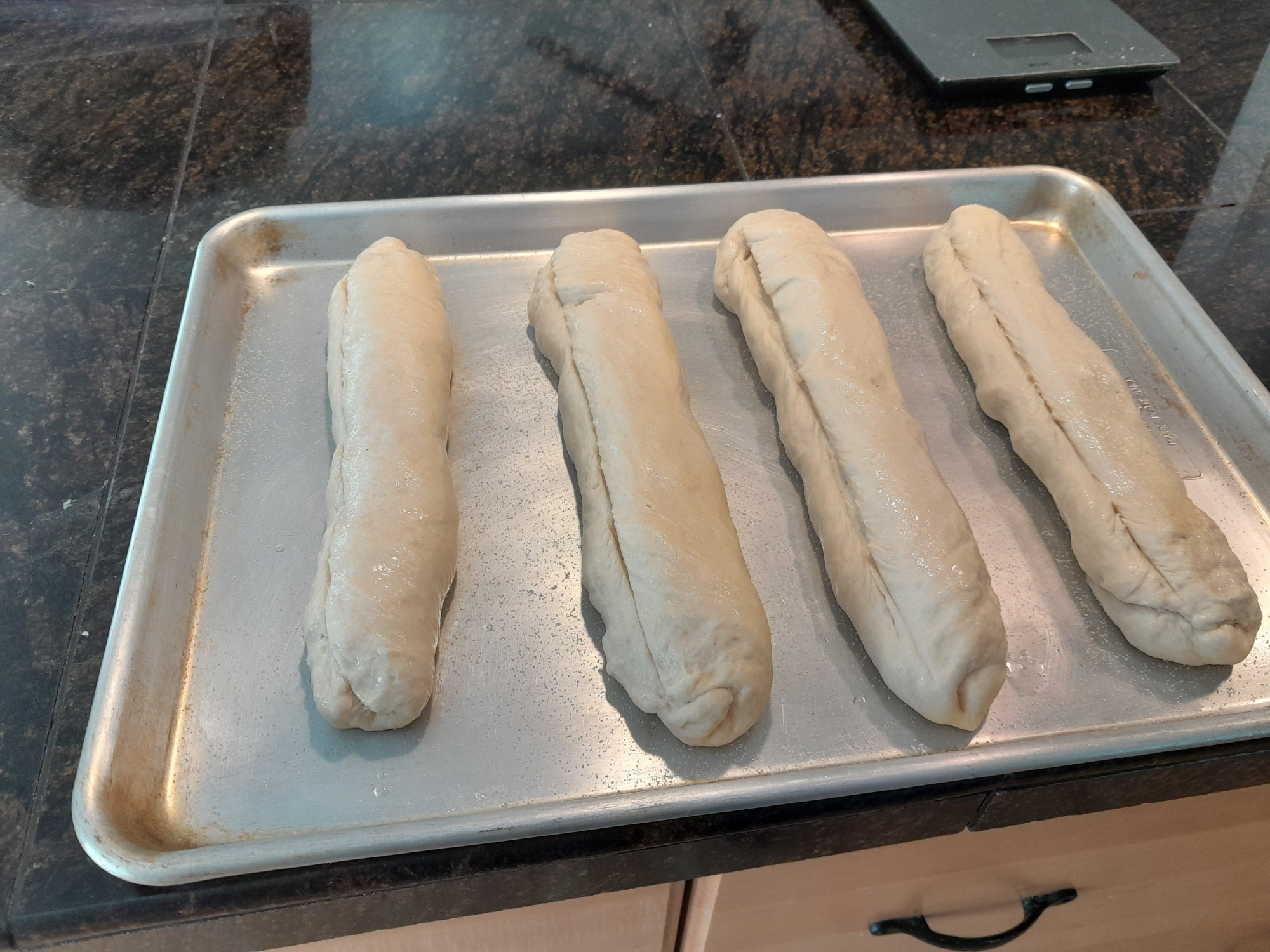 Four unbaked hoagie rolls on a sheet pan