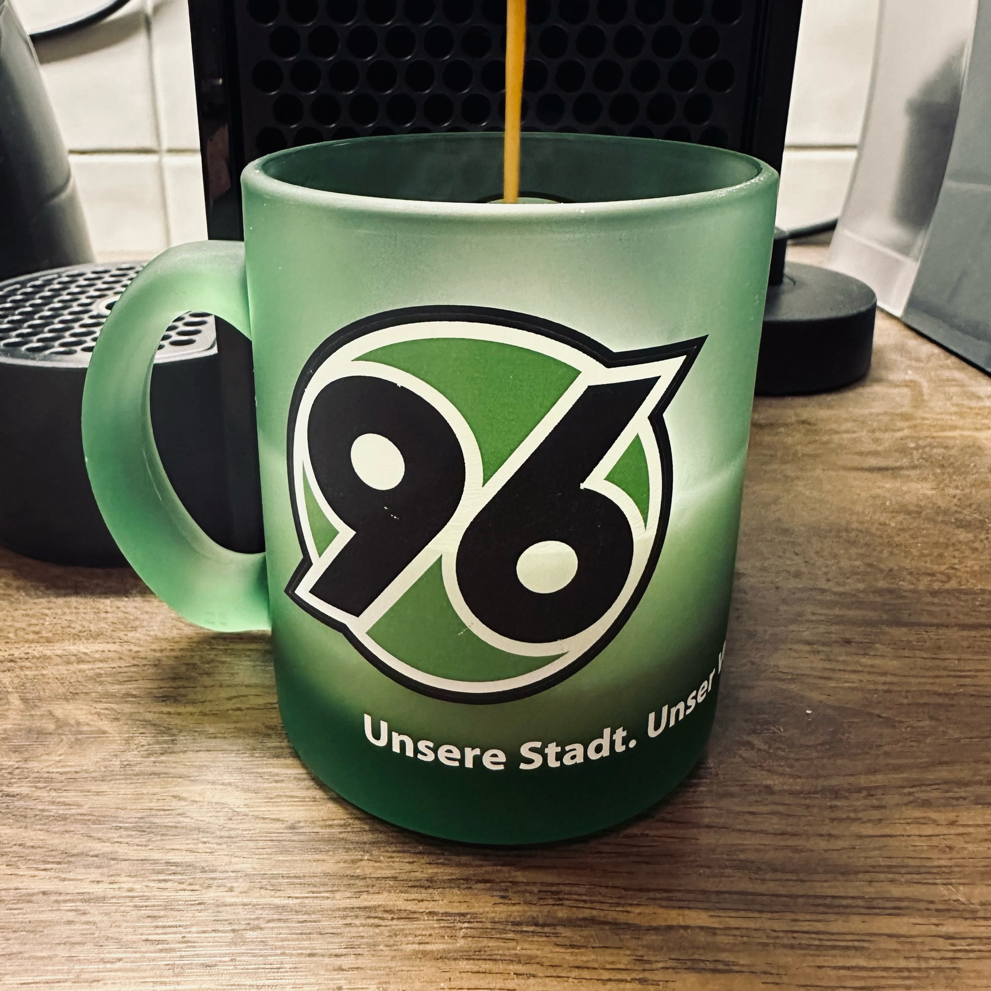 Hannover 96 Kaffeebecher vor einer Kaffeemaschine, in den gerade leckerer Kaffee einläuft.