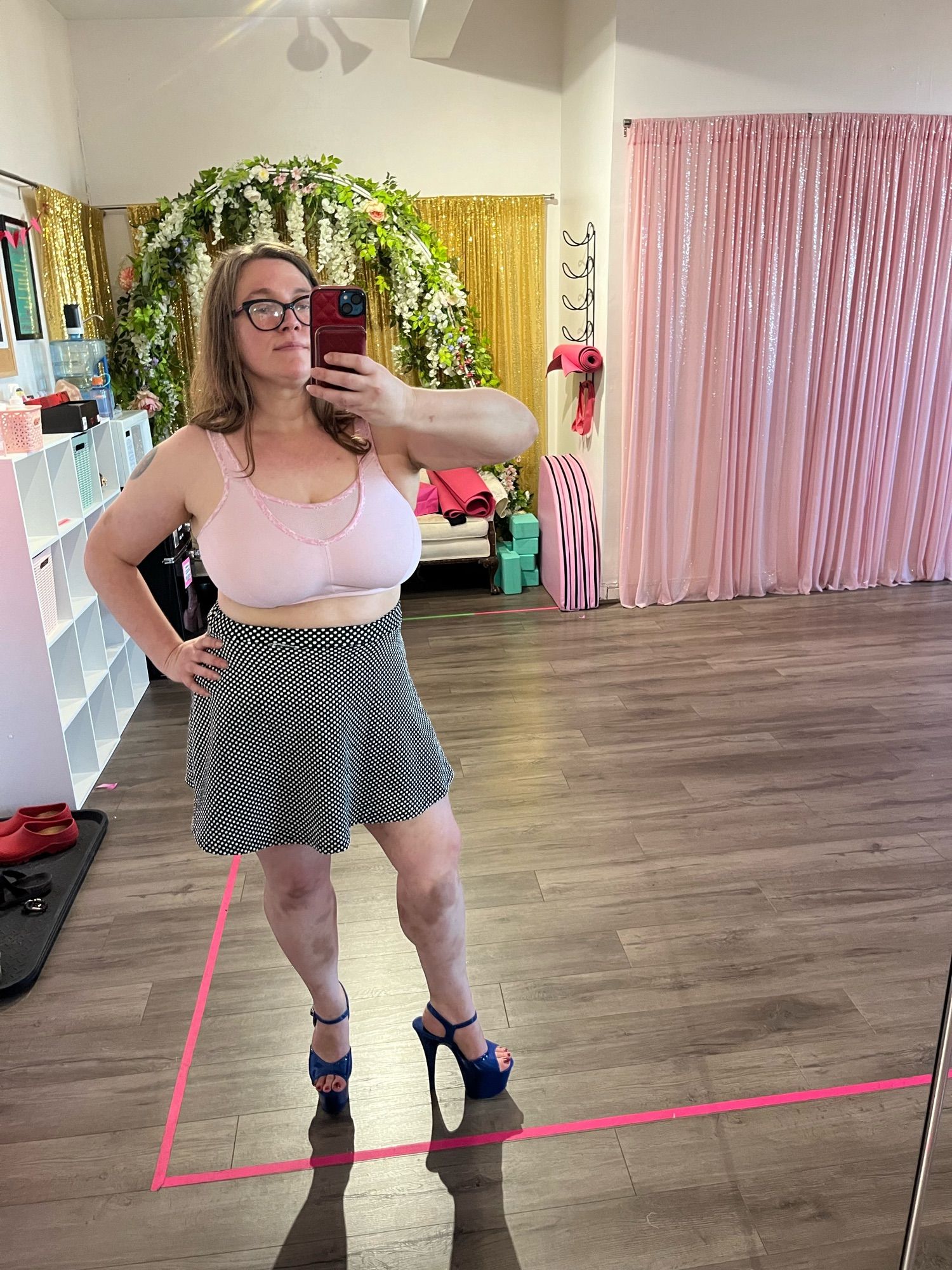 White lady mirror selfie. I’m wearing a pink sports bra, a black above the knee skirt with white polkadots, and 7 inch blue platform heels.