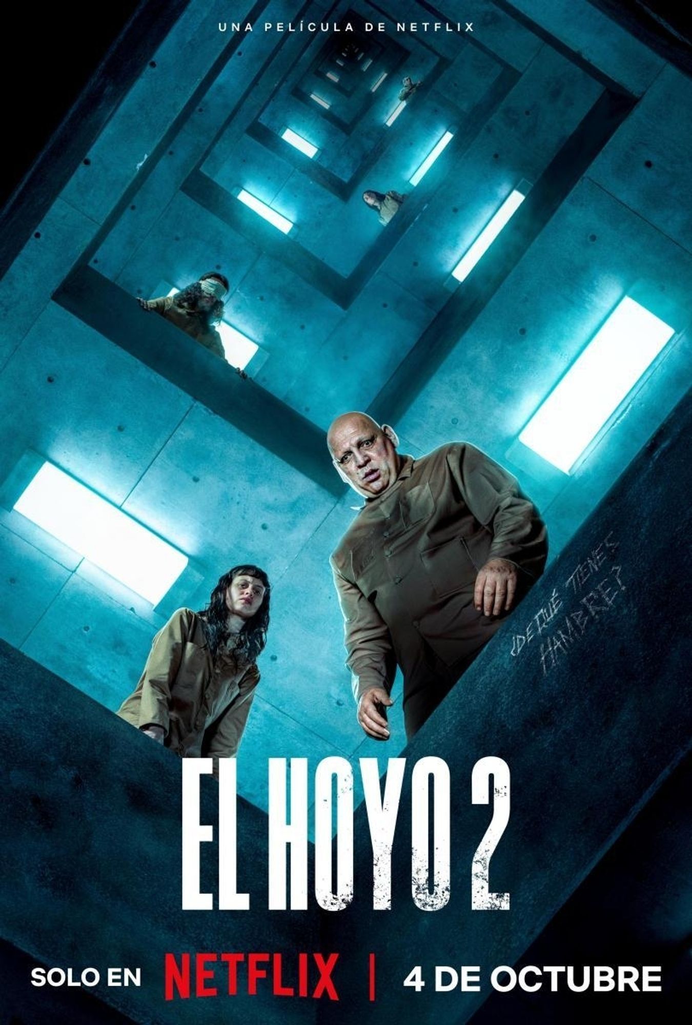 Poster for The Platform 2 with text in Spanish. The view is looking up from an open shaft as a seemingly endless layer of floors stretch above. From the nearest floor a young woman and a bulky man are looking down on you.