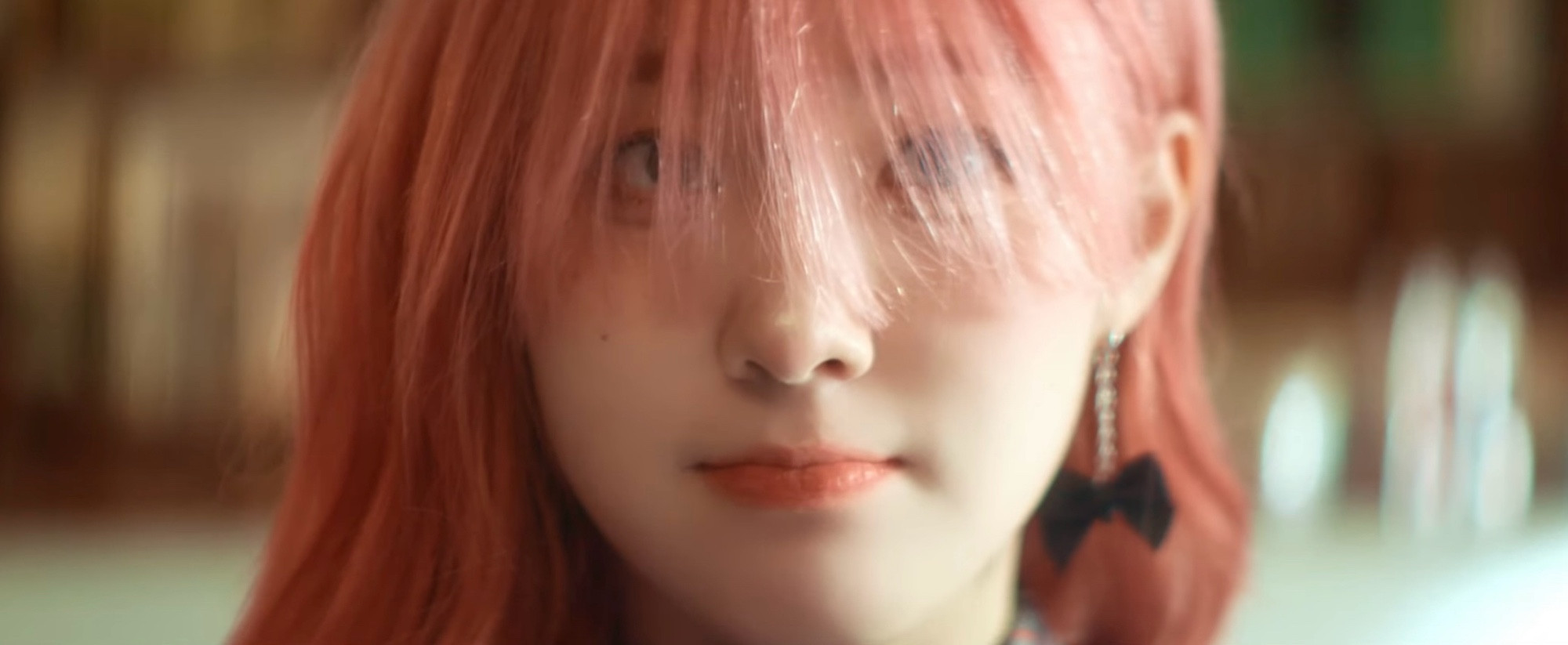 A close up of Kep1er’s Chaehyun with long pink bangs covering her eyes.