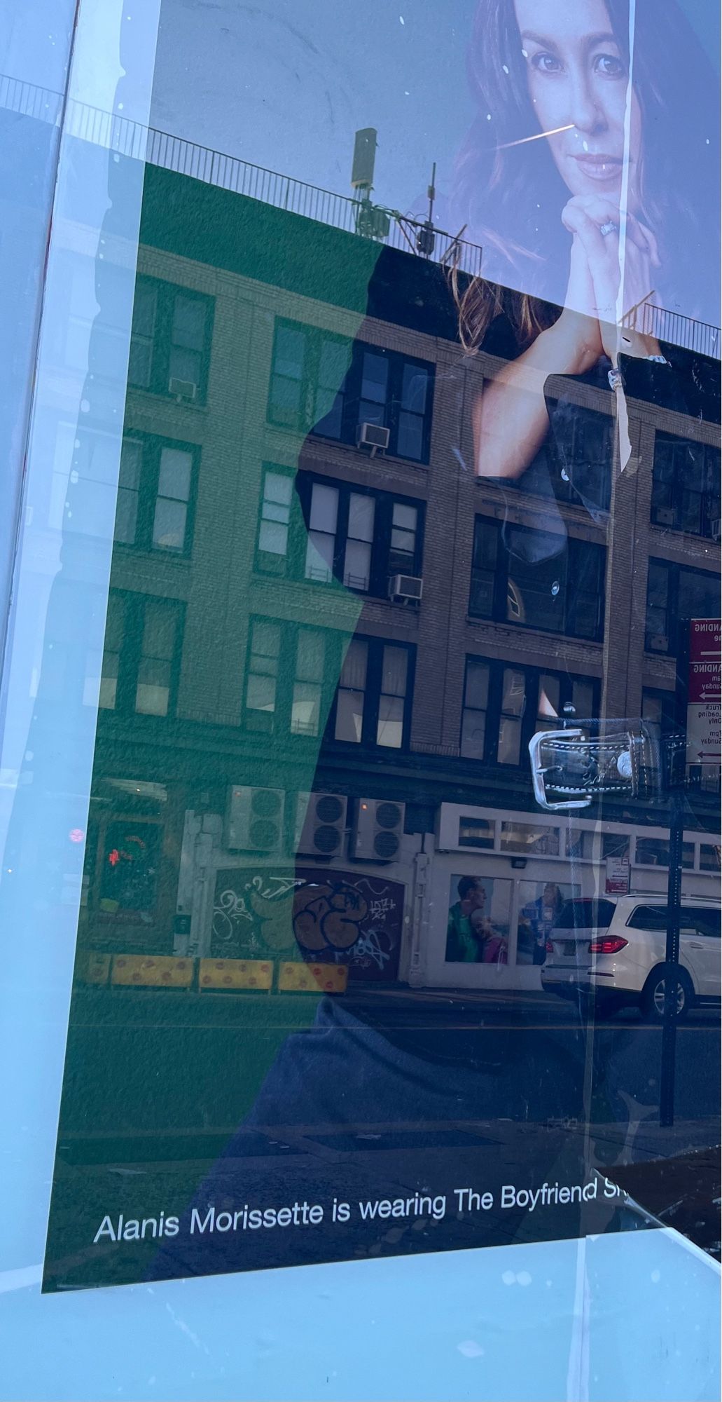 An ad on the window of The Gap. AlanisMorisette is photographed with the caption “Alanis Morisette is wearing the boyfriend shirt.”