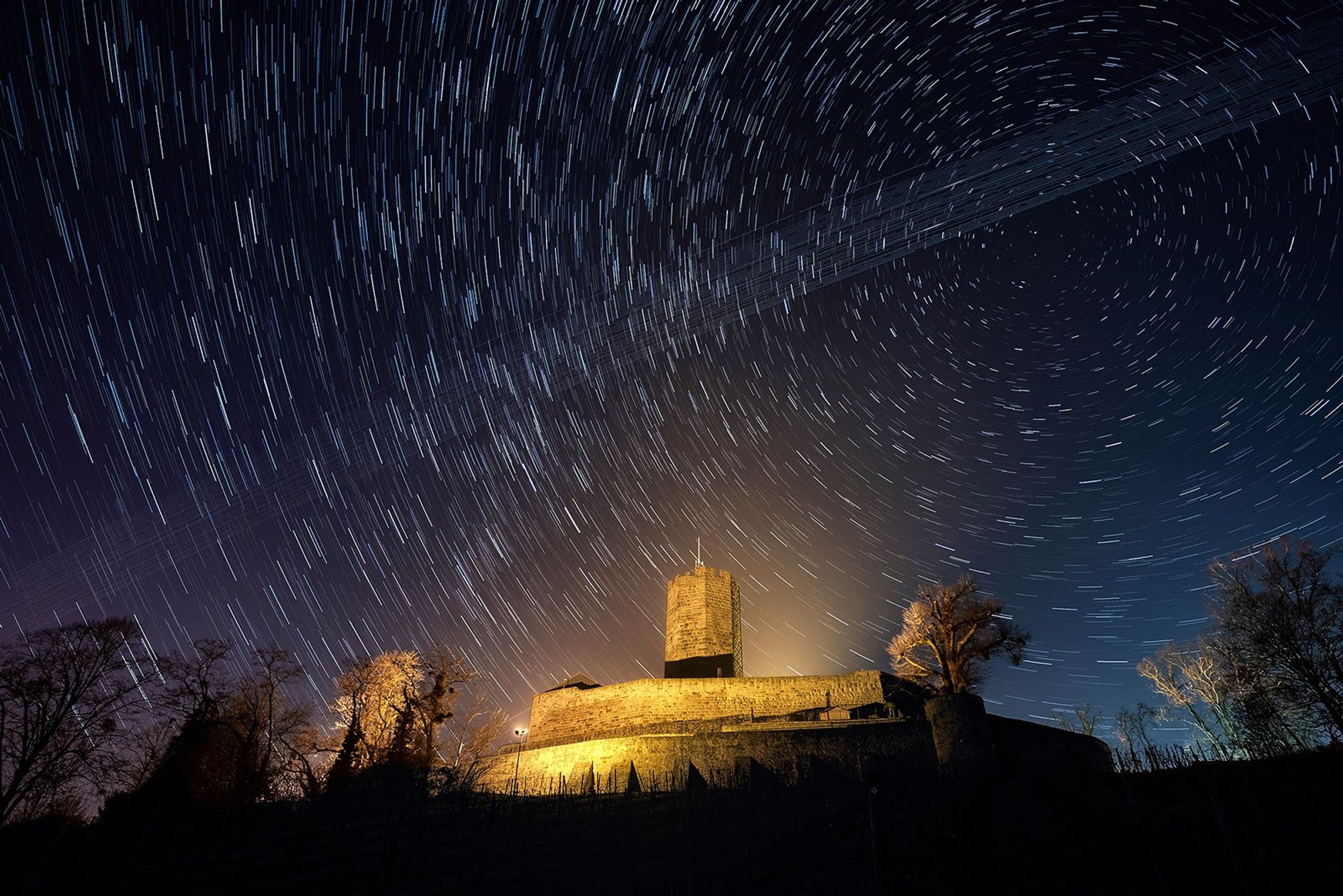 Starlink satellites cross the night sky near a castle