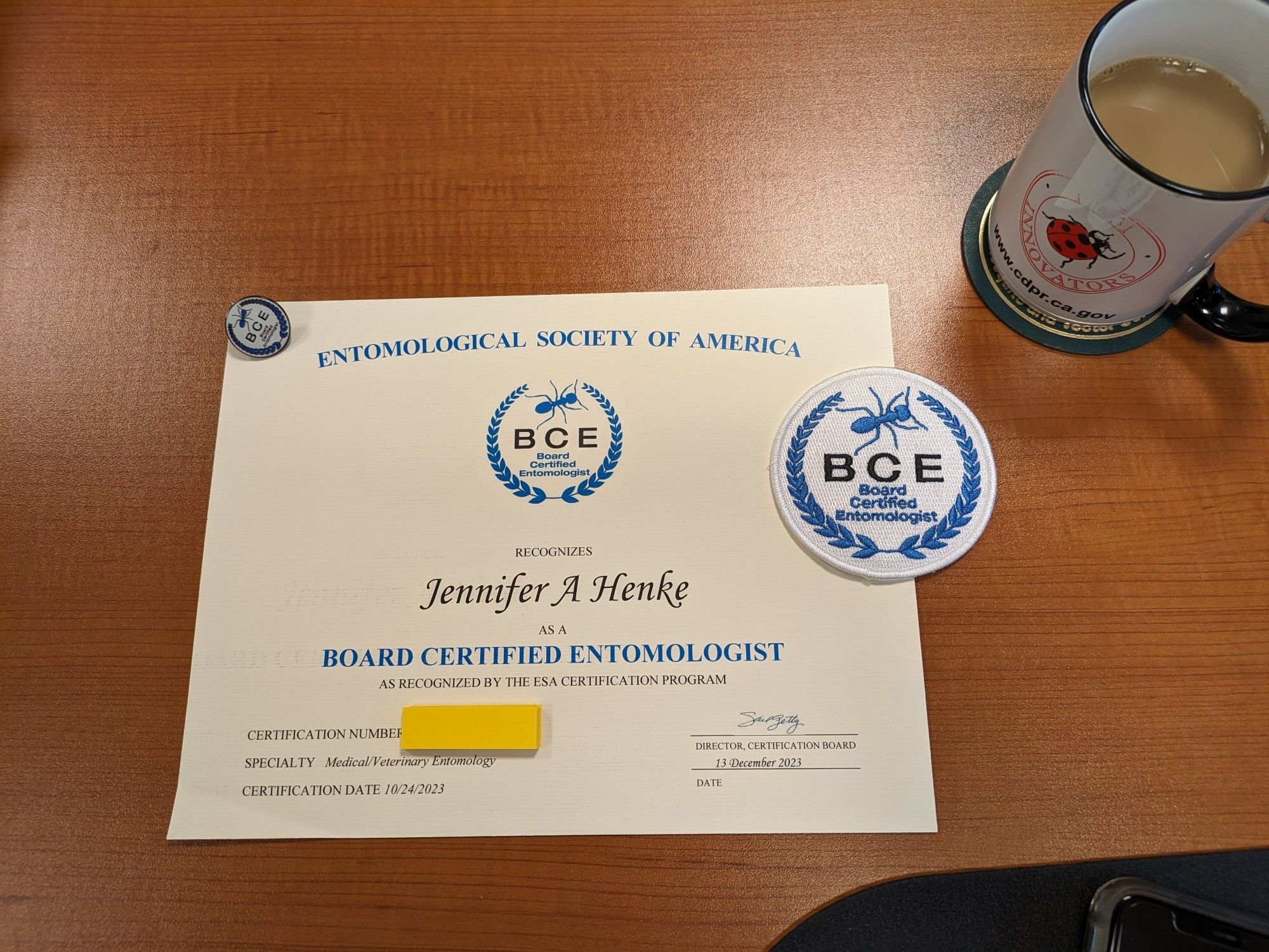 Pin, certificate, and badge of a Board Certified Entomologist with my cup of coffee