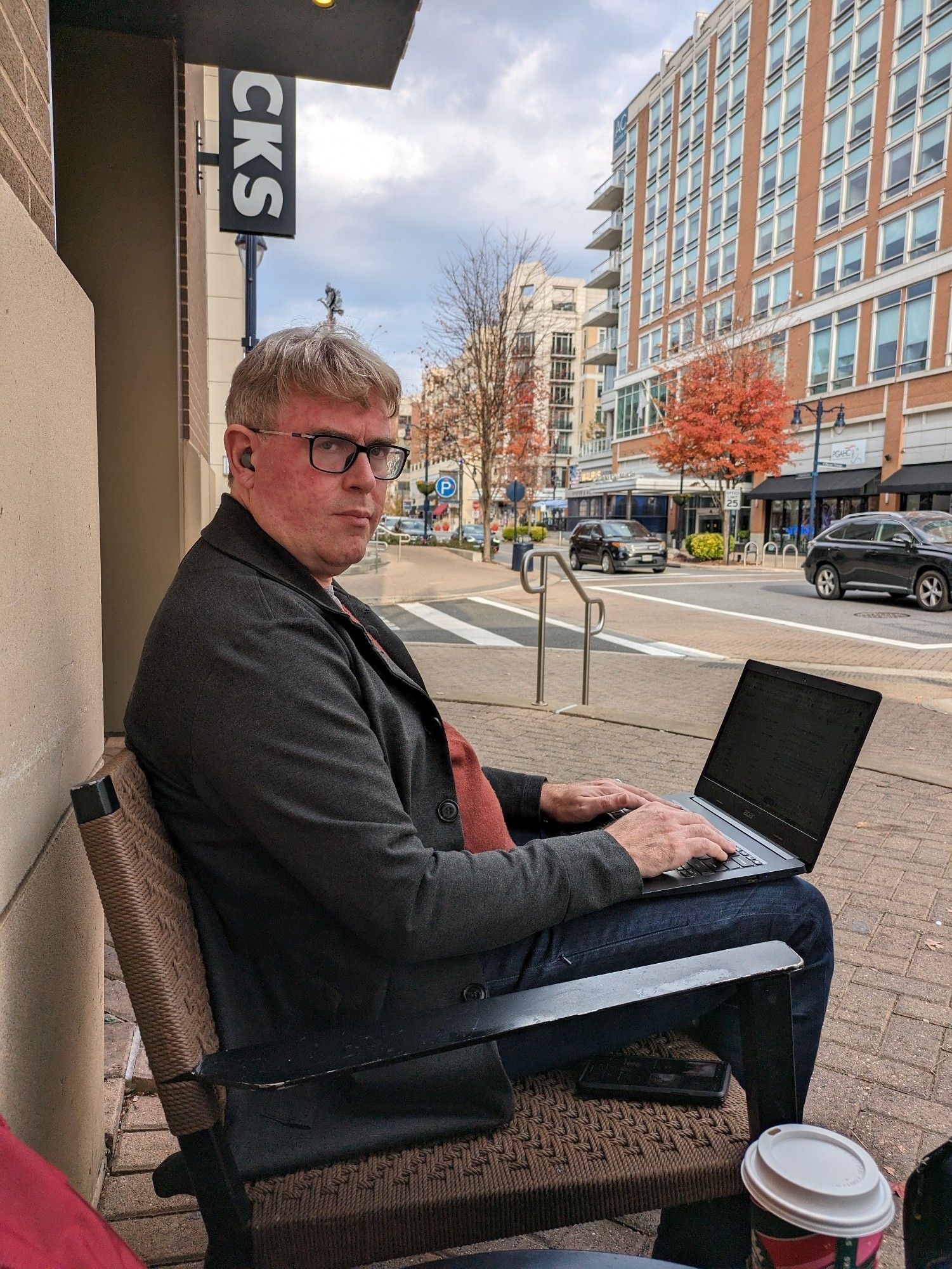 Gareth is a white man sitting outside with his laptop perched on his lap. In the background are cars on the street.