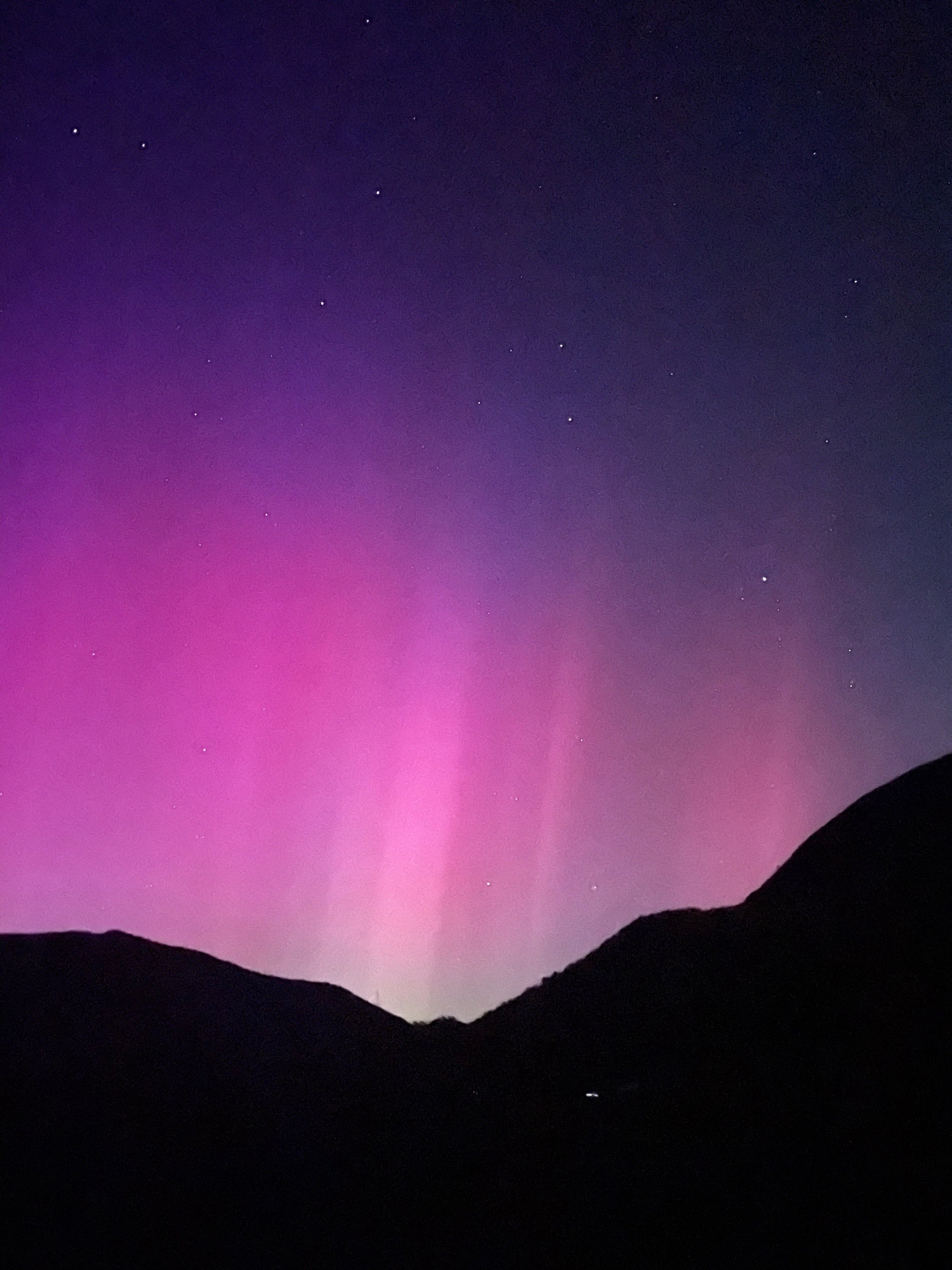 Aurora borealis from green at the horizon (hills) to pinks above, and night sky above that with stars