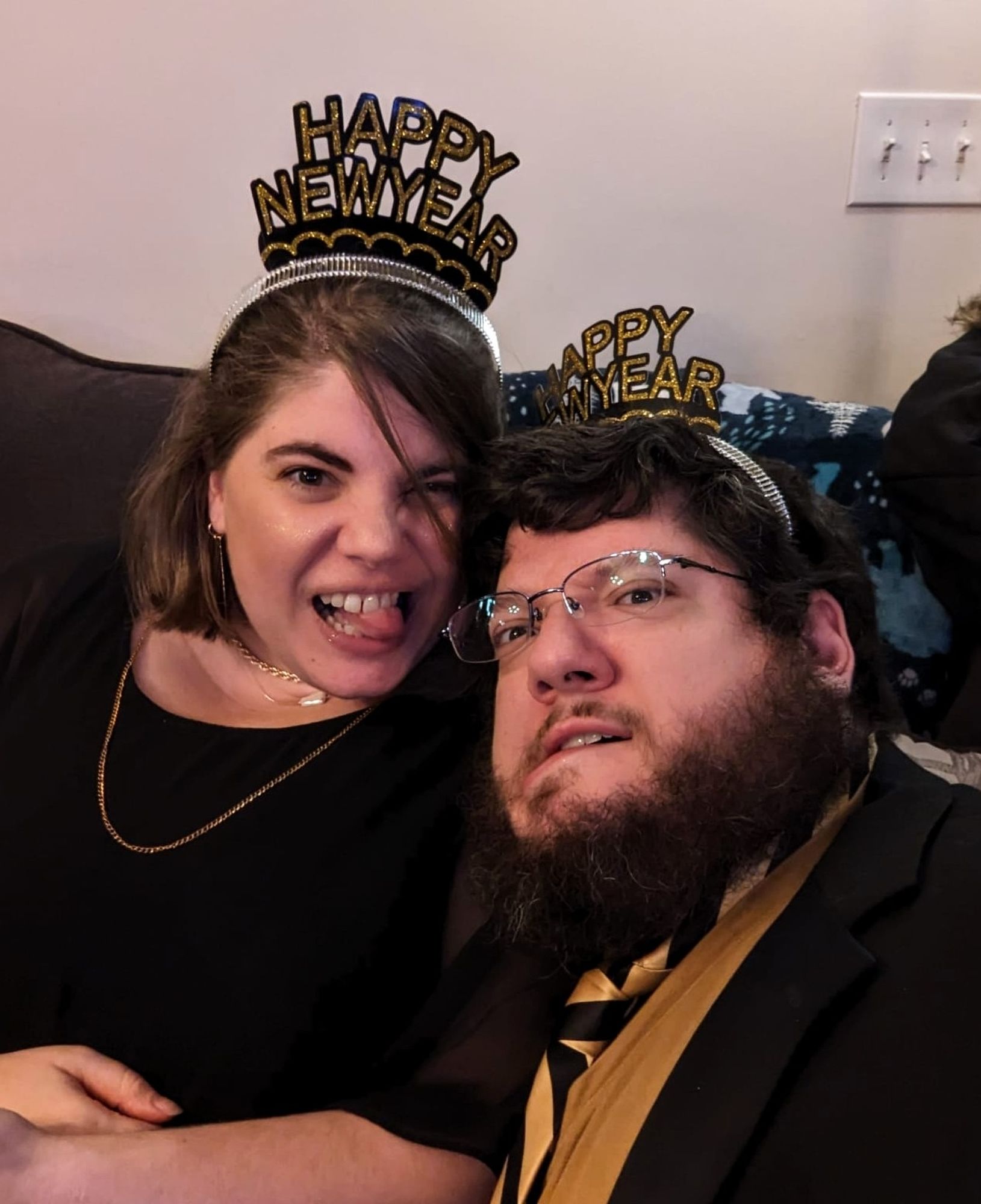 A man and a woman wearing Happy New Year hats and making faces at the camera.