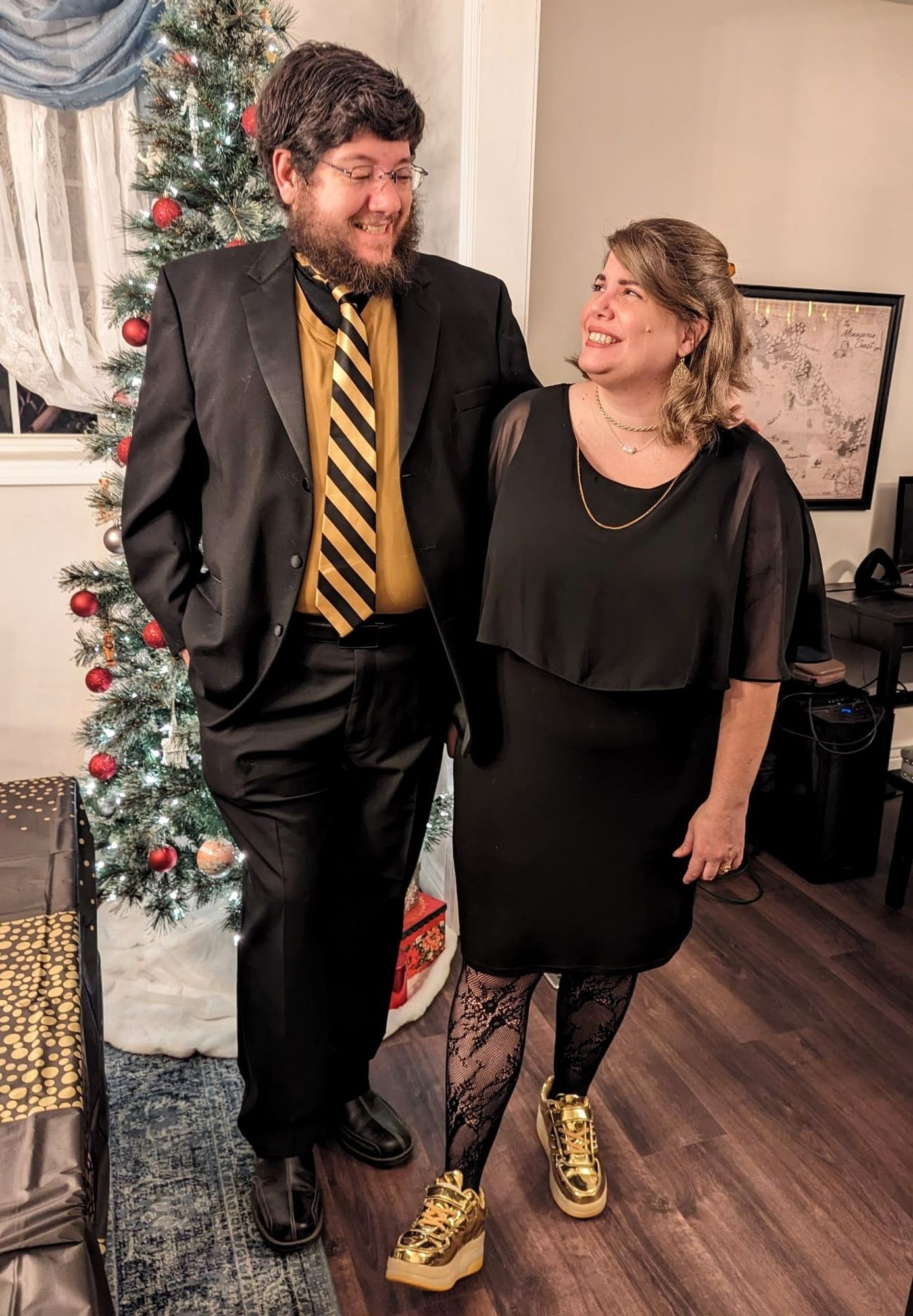 A tall man and shorter woman wearing fancy black and gold outfits.