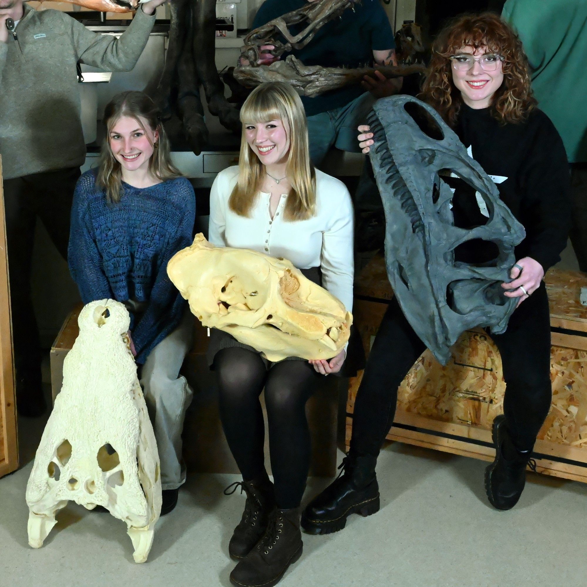 Three women undergraduate researchers are seated and holding skulls. From left, Ellie Faber with American crocodile skull, Grace Vance with male northern elephant seal skull, and Maranda Stricklin with Allosaurus skull.