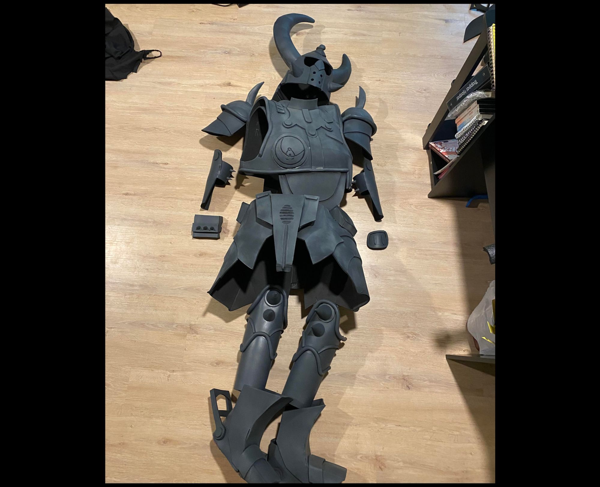 An unpainted suit of EVA foam armor lying loosely assembled on a wooden floor.