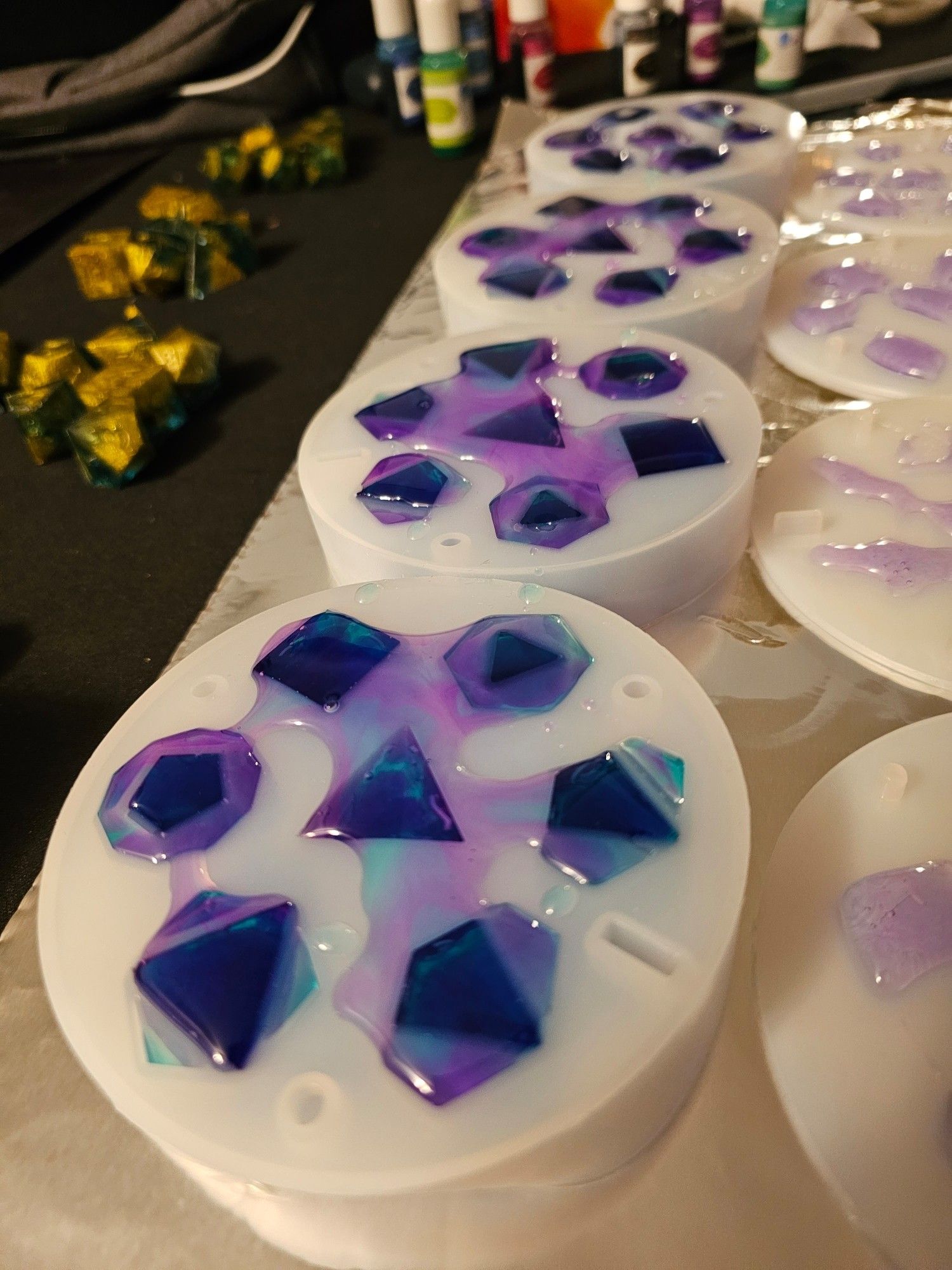 Four polyhedral dice molds lined up on a table, filled with resin