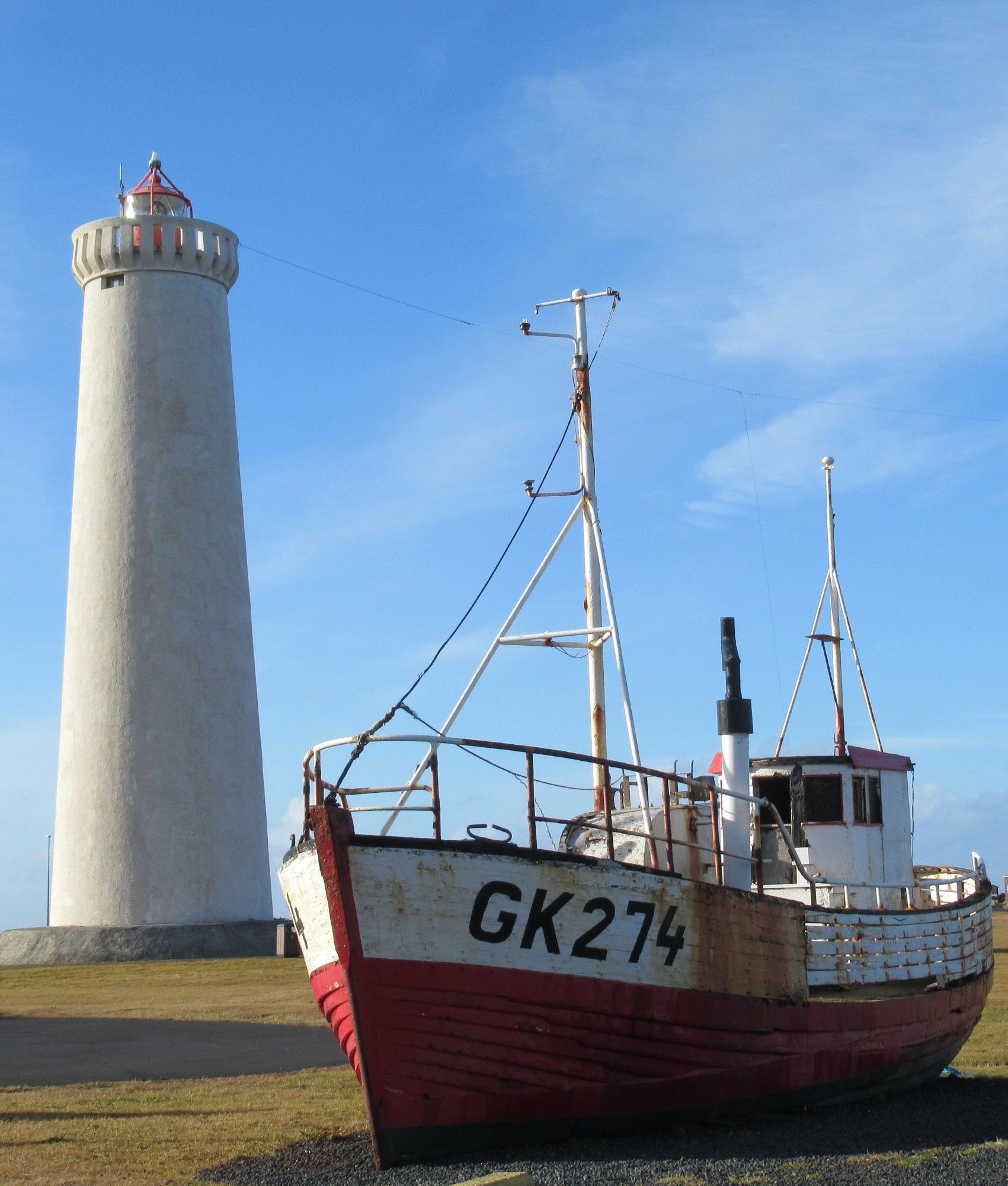 Un phare blanc et un bateau de pêche blanc et rouge abandonné, sous un ciel bleu. Péninsule de Reykjanes, Islande (octobre 2018)