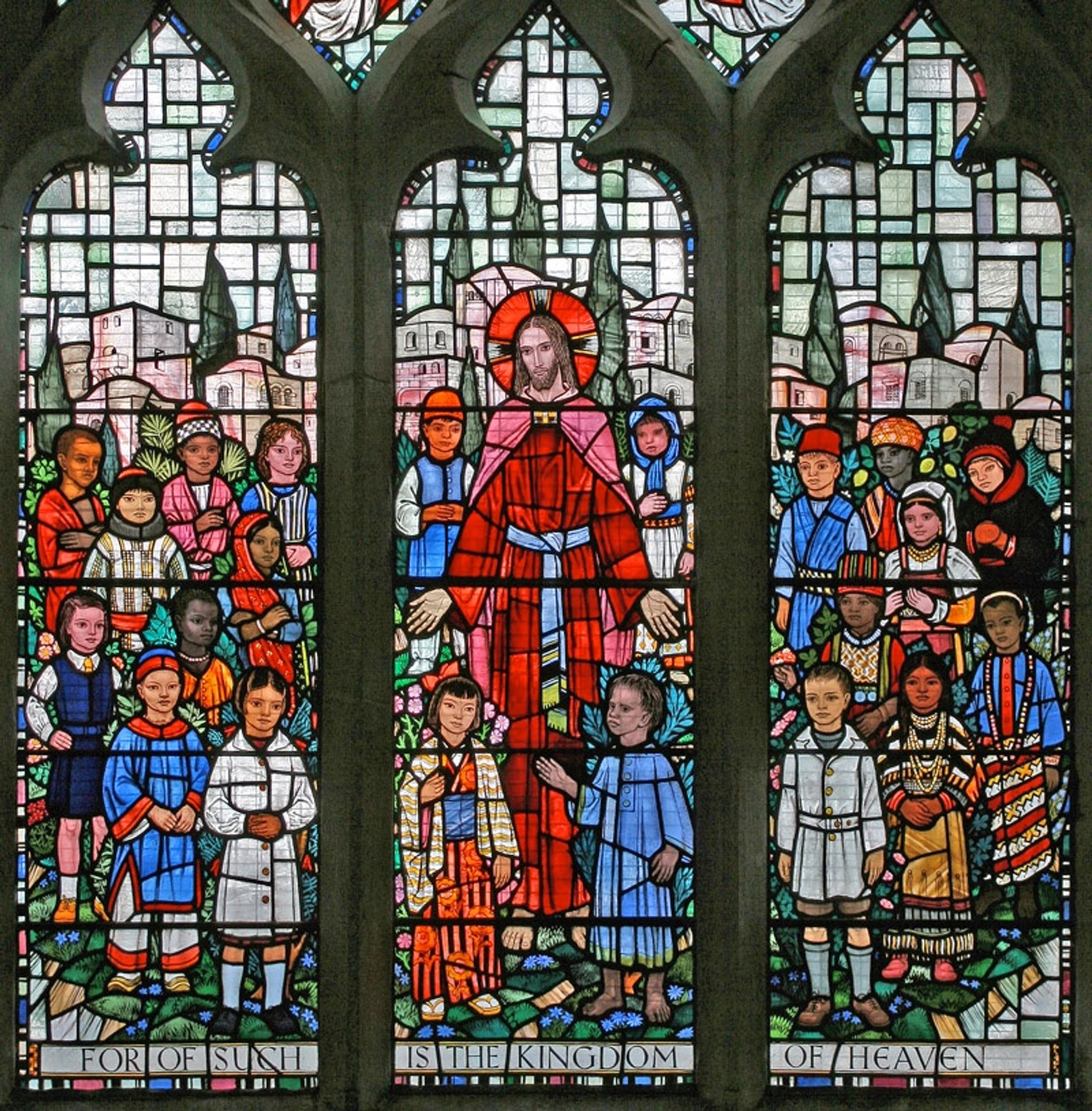 Stained glass window showing the central standing figure of Jesus in a red robe, surrounded by 21 children of different nationalities all dressed in their national costumes. All the figures are looking out at the viewer.