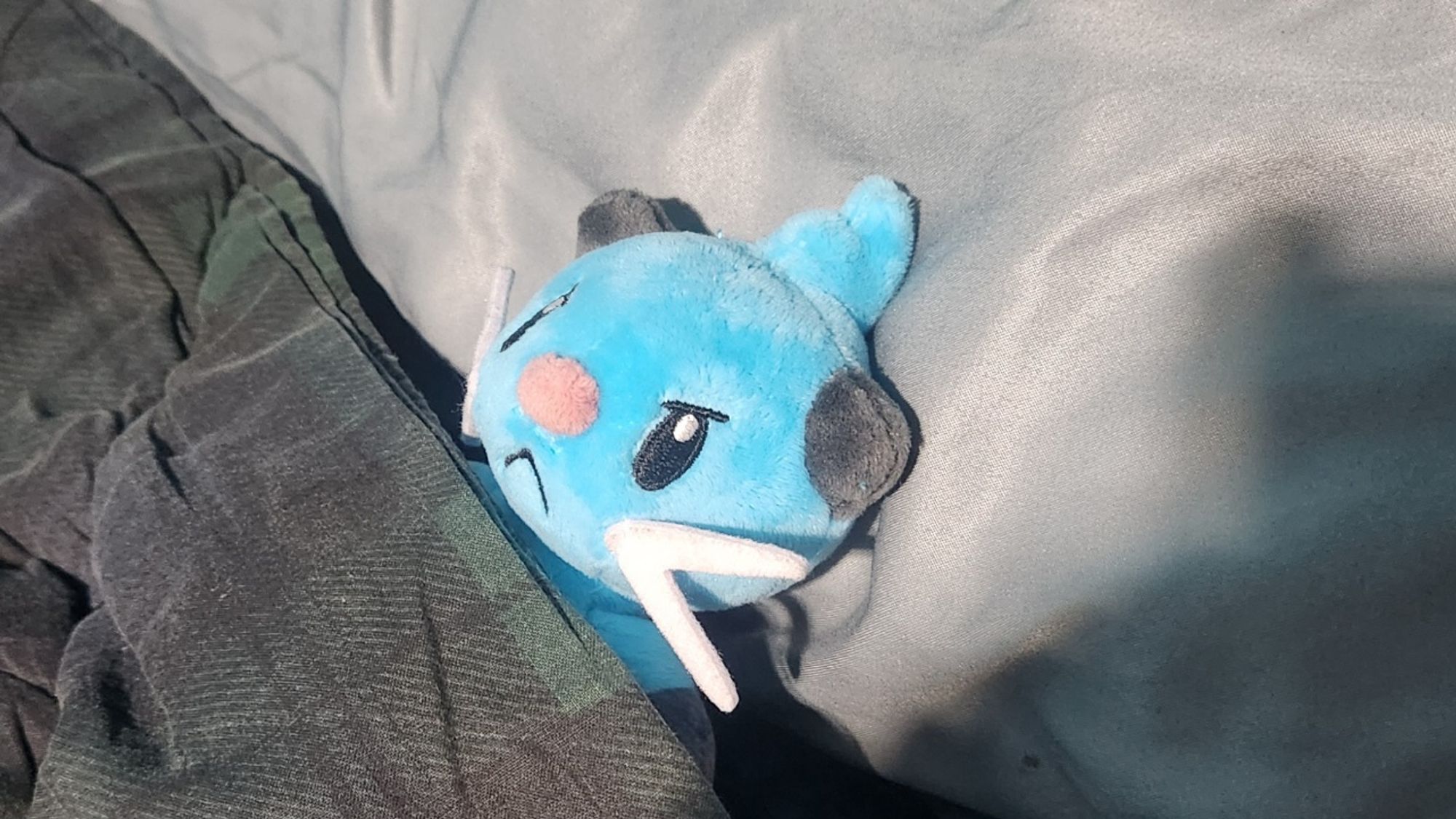 Small plush of an angry blue otter (the Pokémon dewott) tucked in a bed.