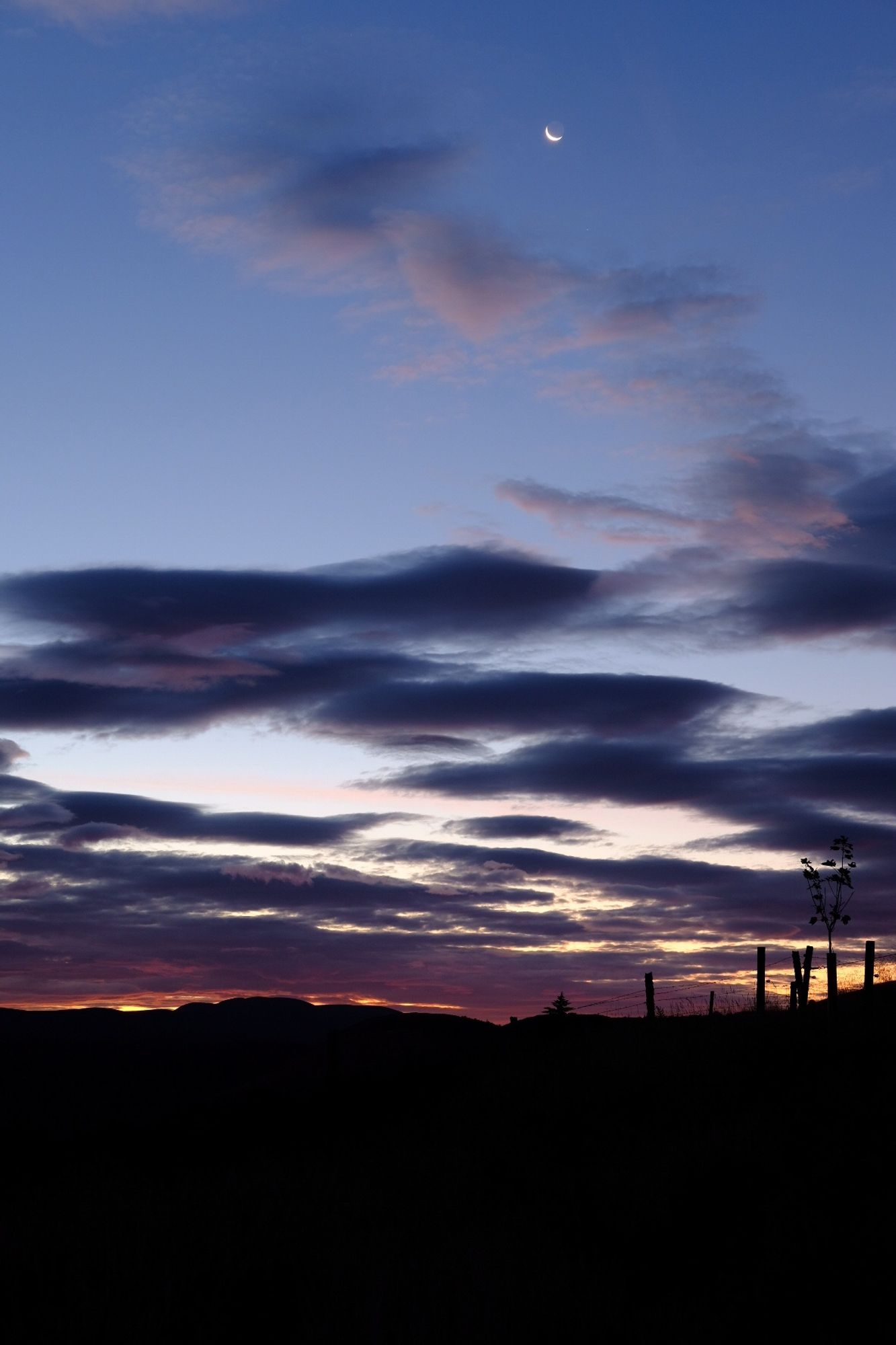 Fiery low sky above a black landscape, moon high above