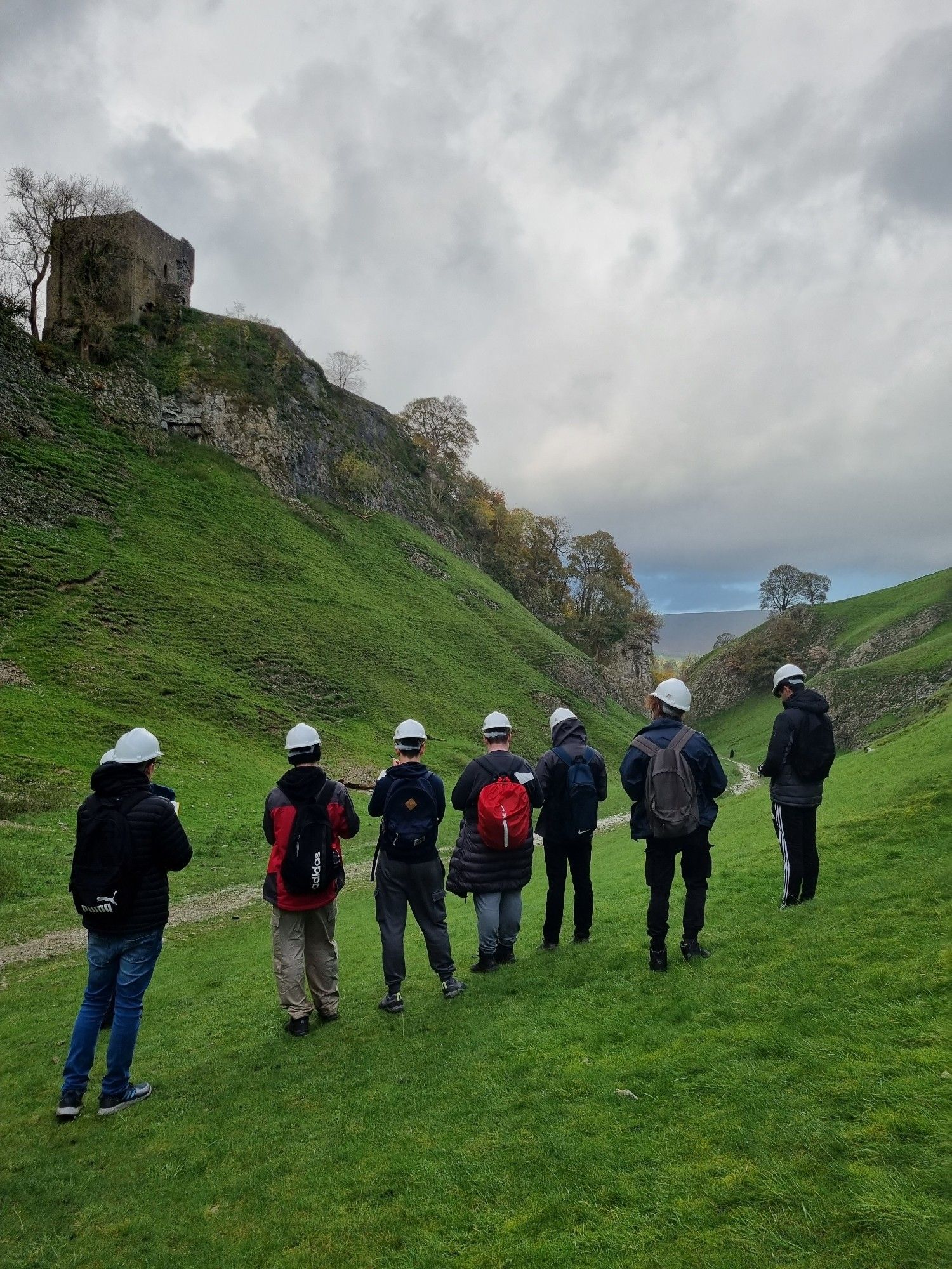 Students make observations of a limestone valley to try to reveal how it was formed. Students stand on green grass, with limestone cliffs and a stone castle in background