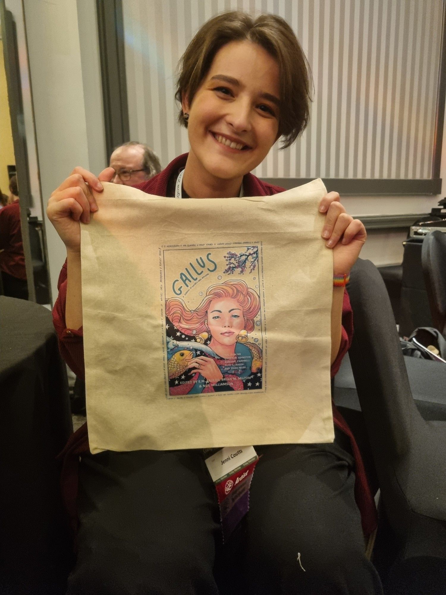 Cover artist and author Jenni Coutts holds a tote bag with the design of her Gallus cover on the front.