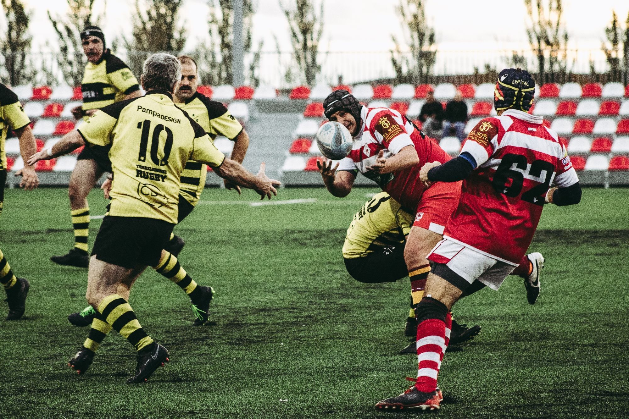 Partido de rugby. Un jugador está siendo placado mientras realiza un pase