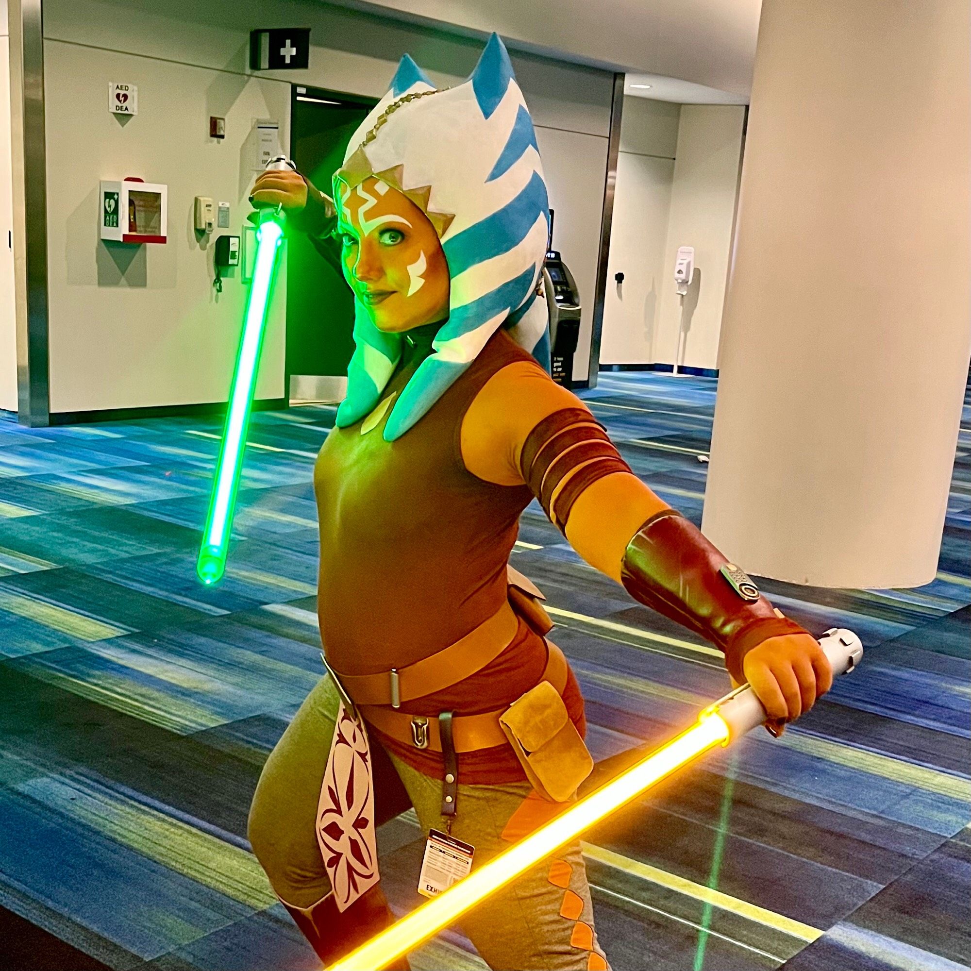 A woman in orange makeup as Asokha the Jedi with her two glowing lightsabers