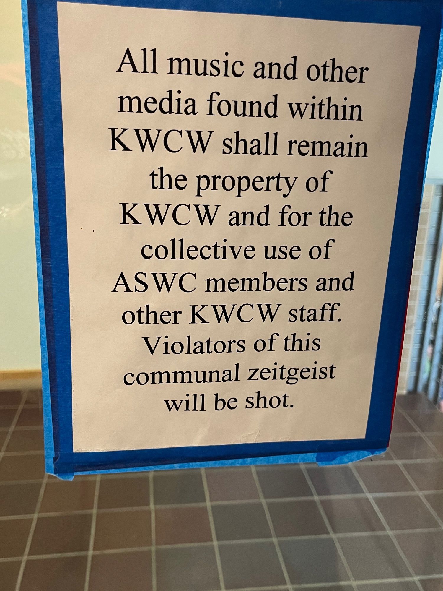 A sign at the KWCW radio studio saying “All music and other media found within KWCW shall remain the property of KWCW and for the collective use of ASWC members and other KWCW staff. Violators of this communal zeitgeist will be shot.”