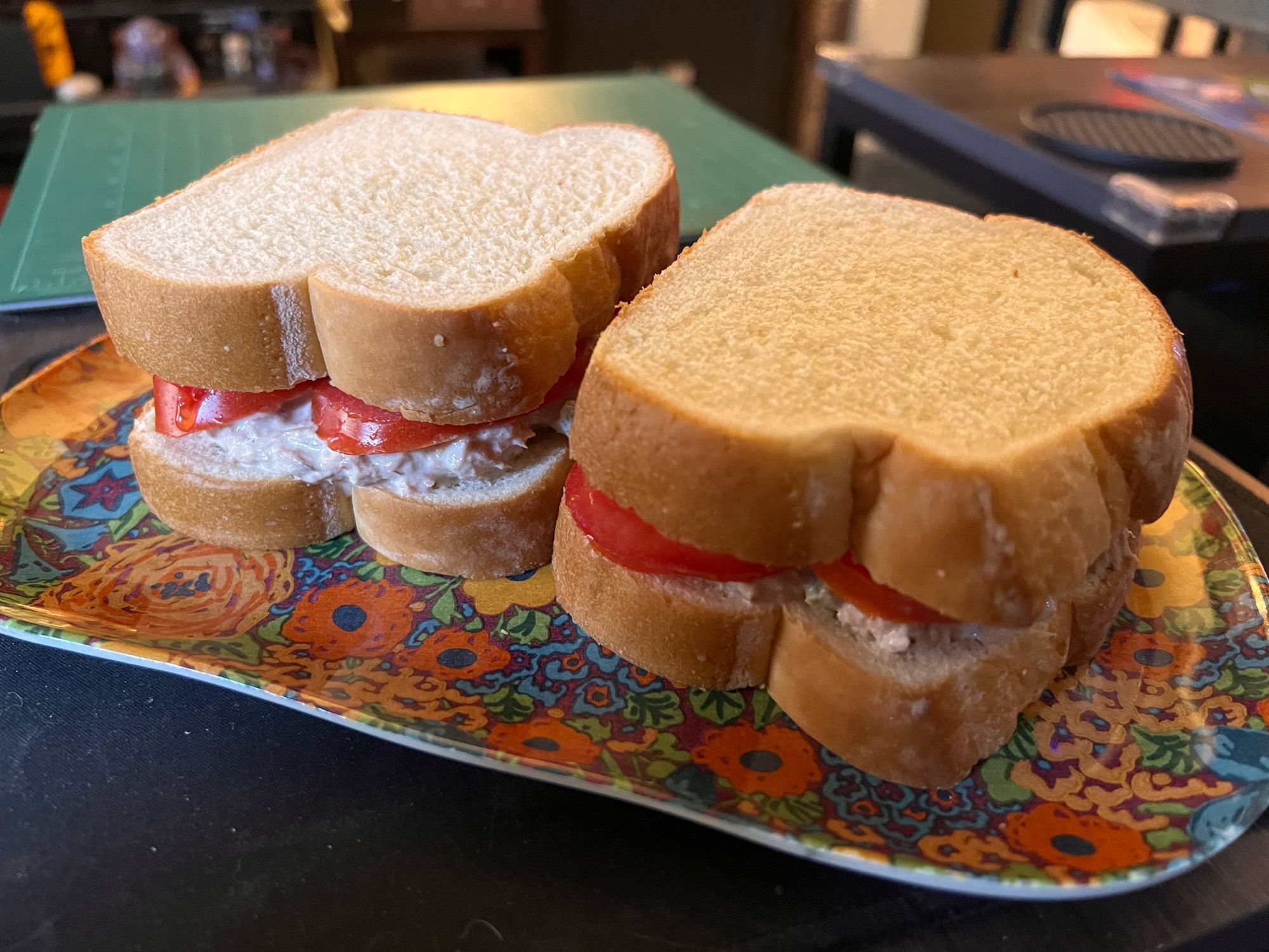 two tuna salad sandwiches on white bread with tomato slices, all on a colorful floral plate