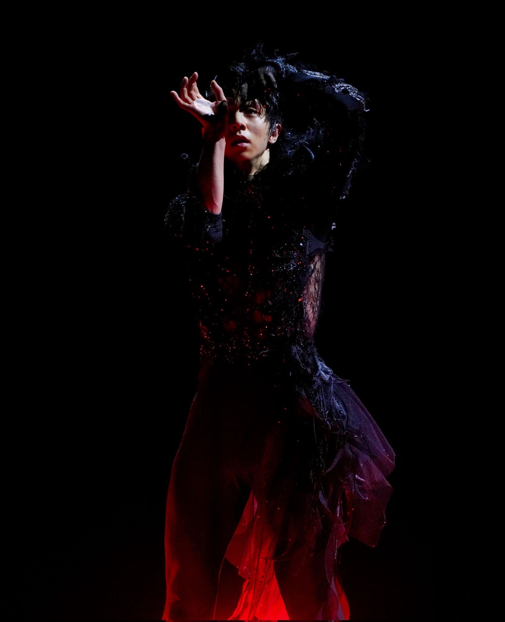 Yuzuru Hanyu in his GOL costume surrounded by darkness with a spotlight shining harshly on him from above.