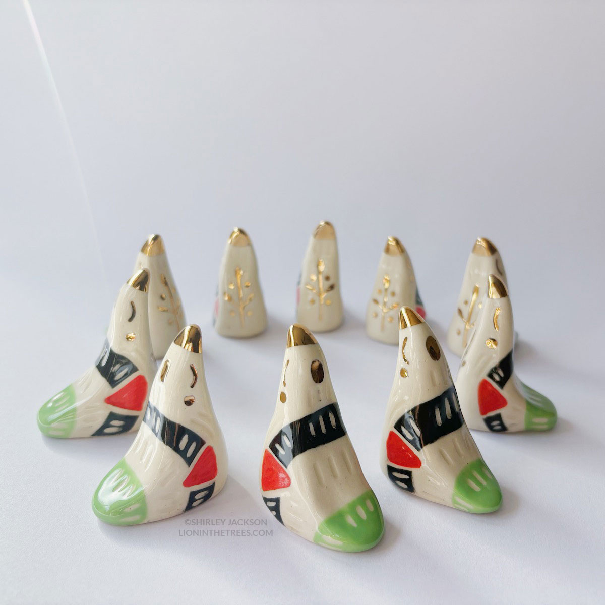 Dove totems done with black, red, and green underglazes that mimic the Palestinian flag; finished with clear glaze and gold overglaze details such as an olive tree branch motif. These totems have been arranged in a circular formation.