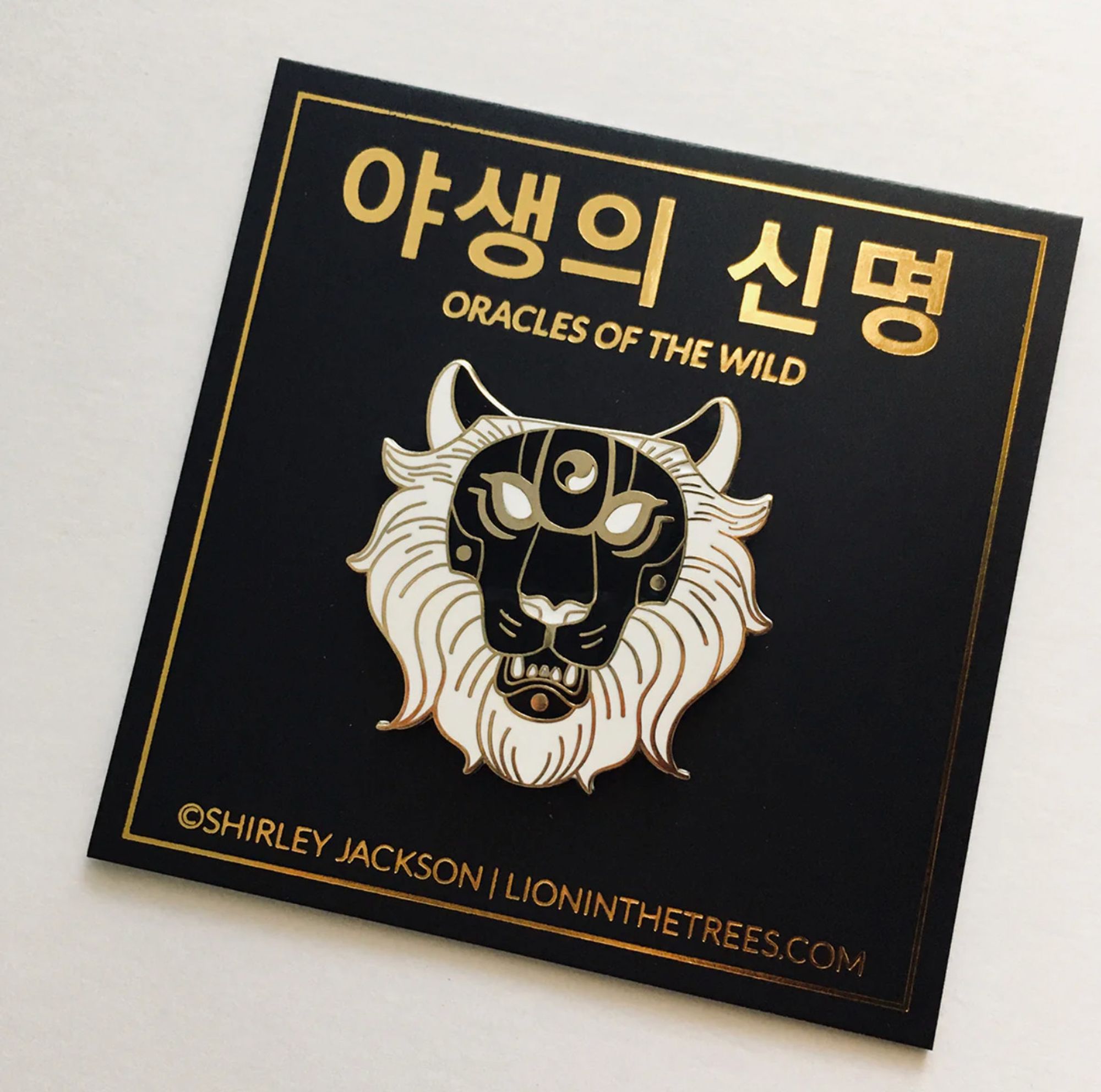 Oracles of the Wild The Crown enamel pin. A black, gold, and white enamel pin designed to look like a lion mask.