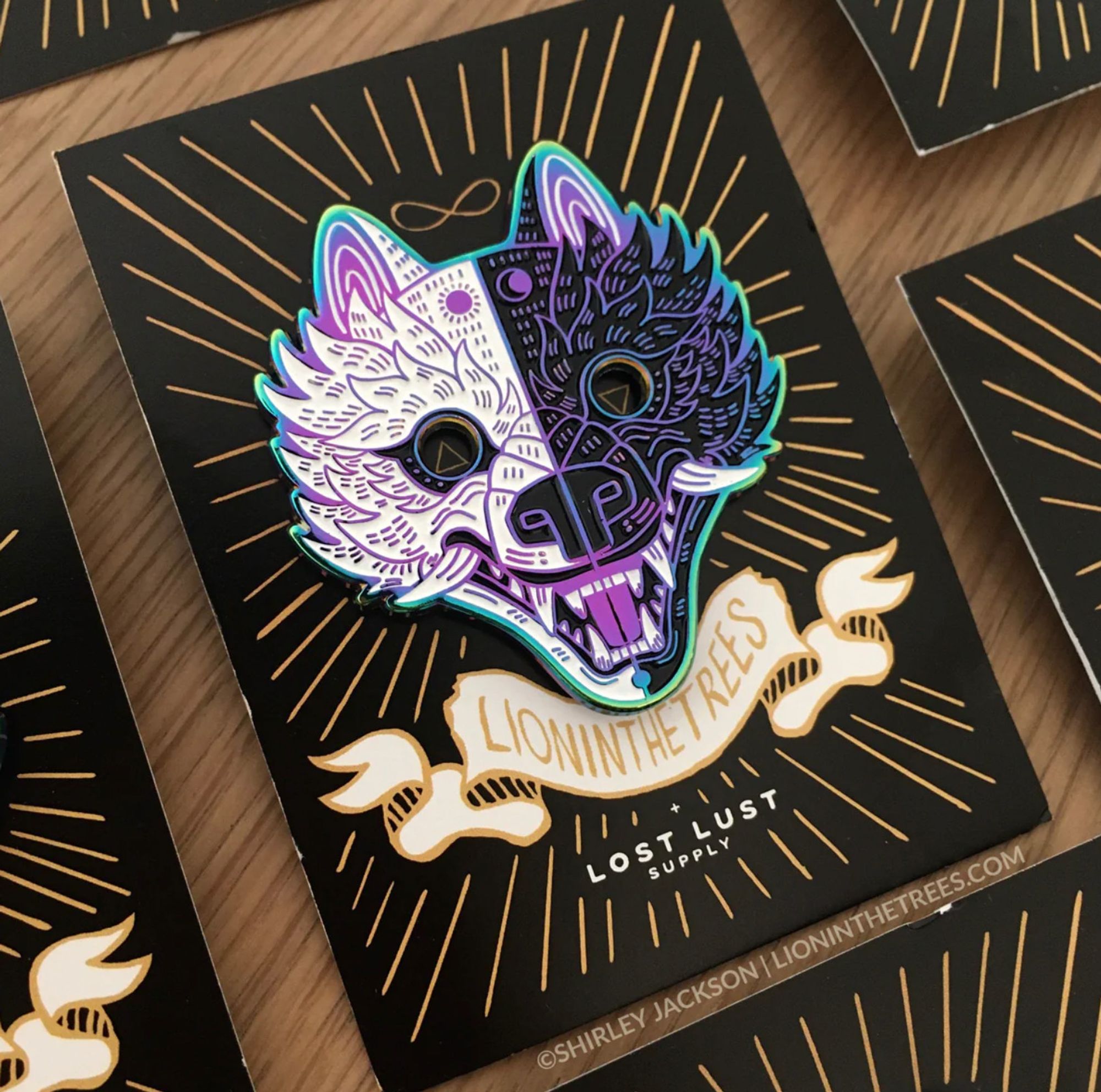 Stay Wild Enamel Pin product (rainbow metal variant) - a wolf head split in half with one side being white with a sun forehead marking and the other is black with a crescent moon forehead marking.