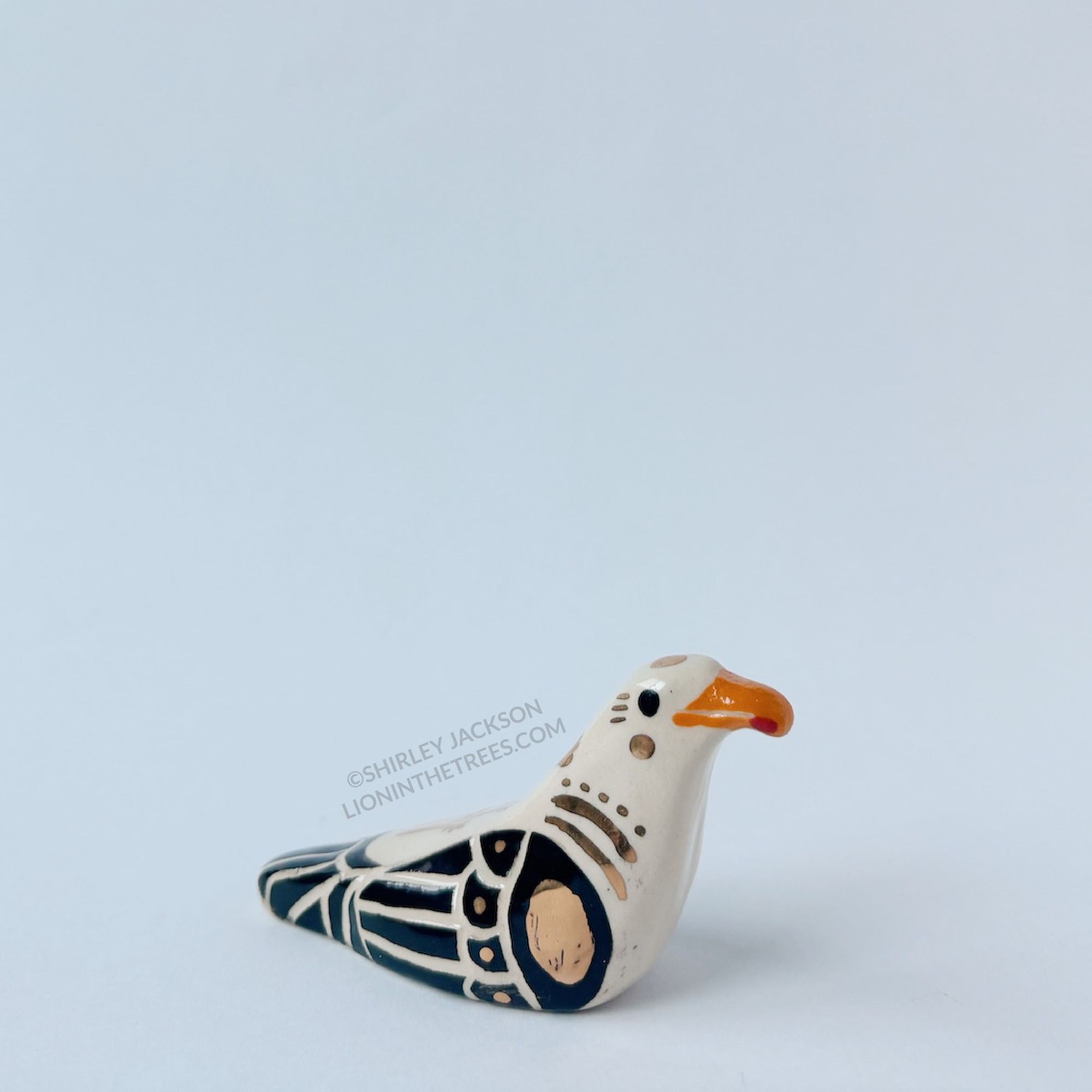 A sculpture that resembles a Seagull done with black and orange underglaze and gold overglaze.