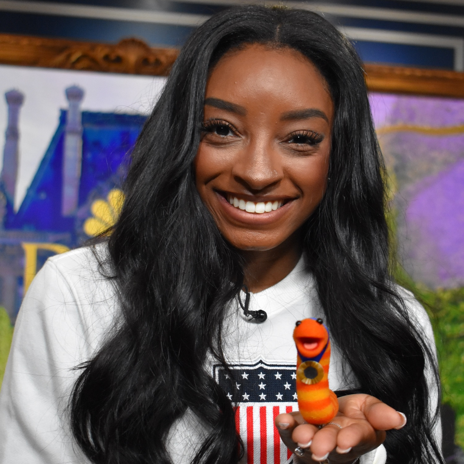 Slimey the worm is a character from Sesame Street. He is an orange and yellow striped worm and so small he can fit in the palm of your hand.
Here he is pictured with the GOAT of gymnastics—Simone Biles.
Slimey is pictured here with a gold medal of his own so this guy is also athletic af!!