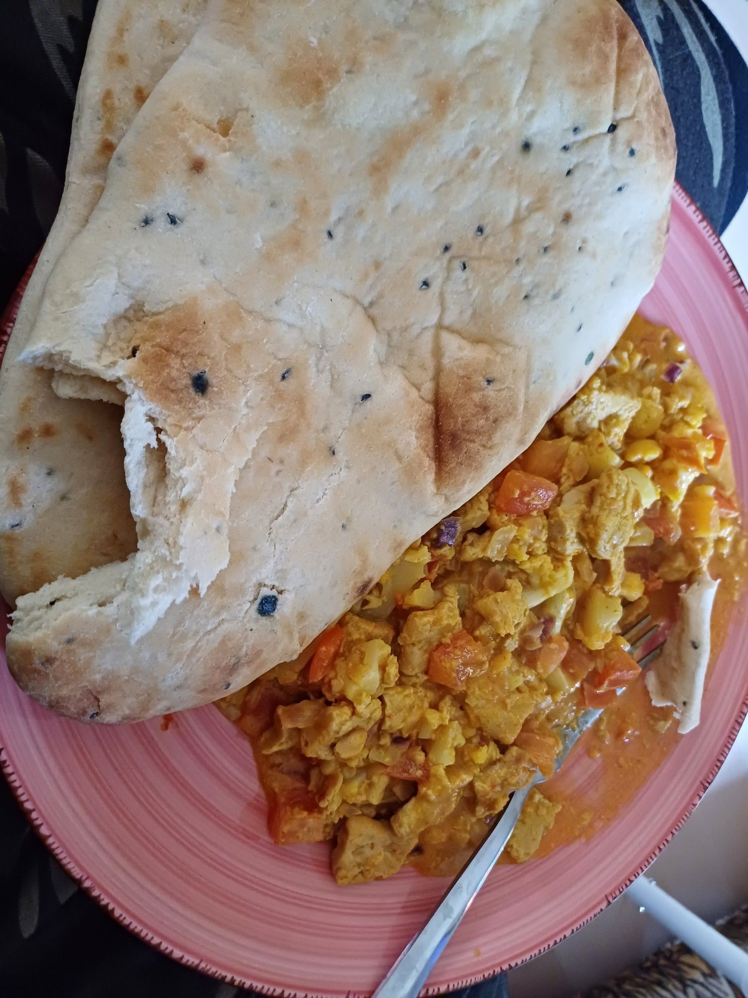 Oudroze gestreept rond bord met een vork, curry en Naanbrood er op.