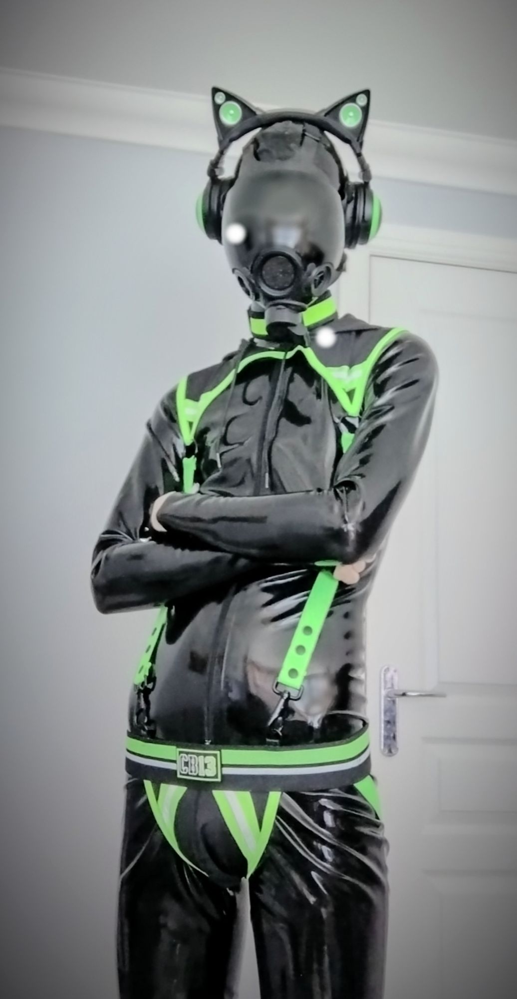 Me standing with my arms crossed. I am wearing a gas mask with green cat ears, a green harness and green jockstrap.