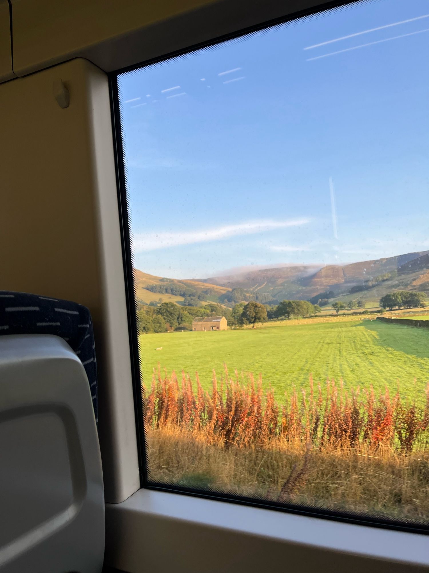 A view of blue sky and sunny fields and hills through a train window