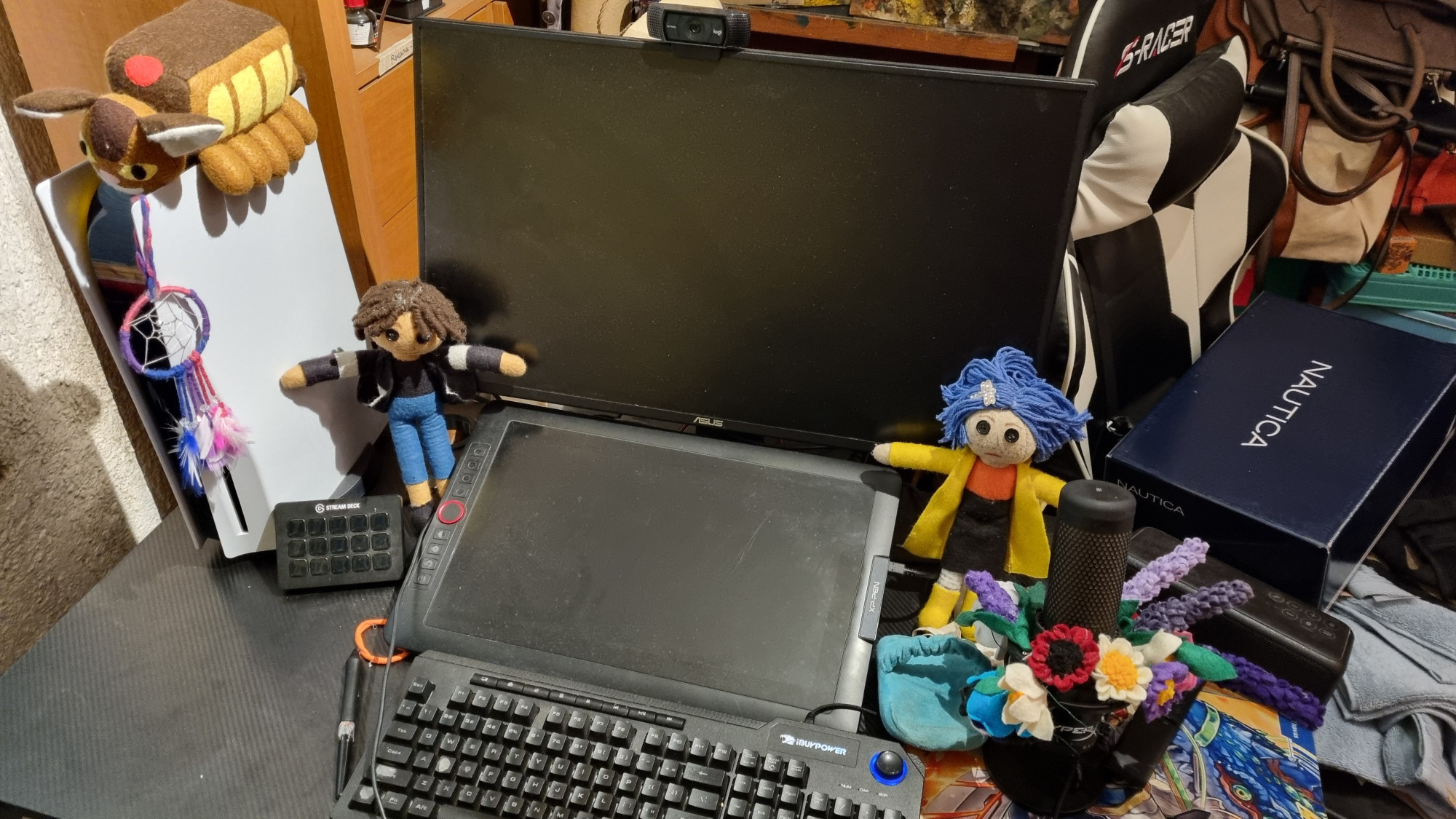 Picture of a desk with two monitors, a microphone and a ps5, flanking the main monitor are two plushies of Wybie and Coraline..the microphone is decorated with felt flowers of many colors and shapes and on the PS5 is a dream catcher as well as a plushie of Catbus from My Neighbor Tototo