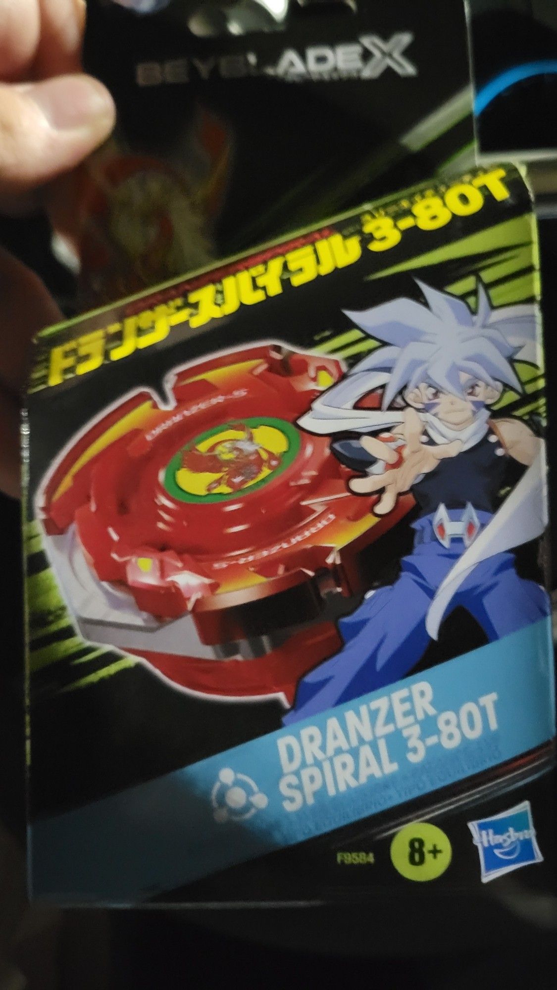 A photo of the packaging of Dranzer Spiral 3-80T From Beyblade's X line. Features art of the character Kai from the first beyblade series, next to a red version of his top of choice, Dranzer.