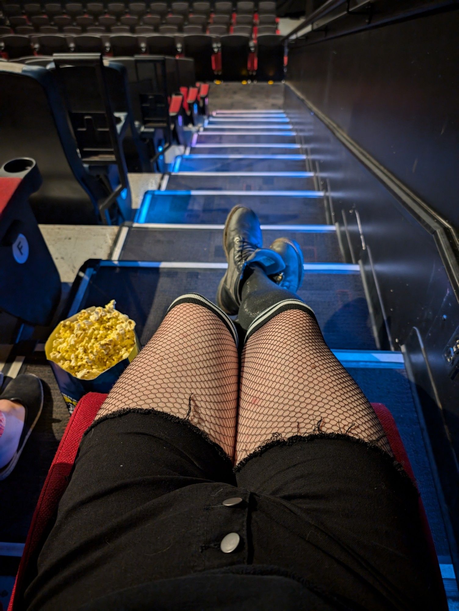 Picture of legs in fishnets with Kneehigh, striped socks and black shorts, in a cinema chair with popcorn on the side.