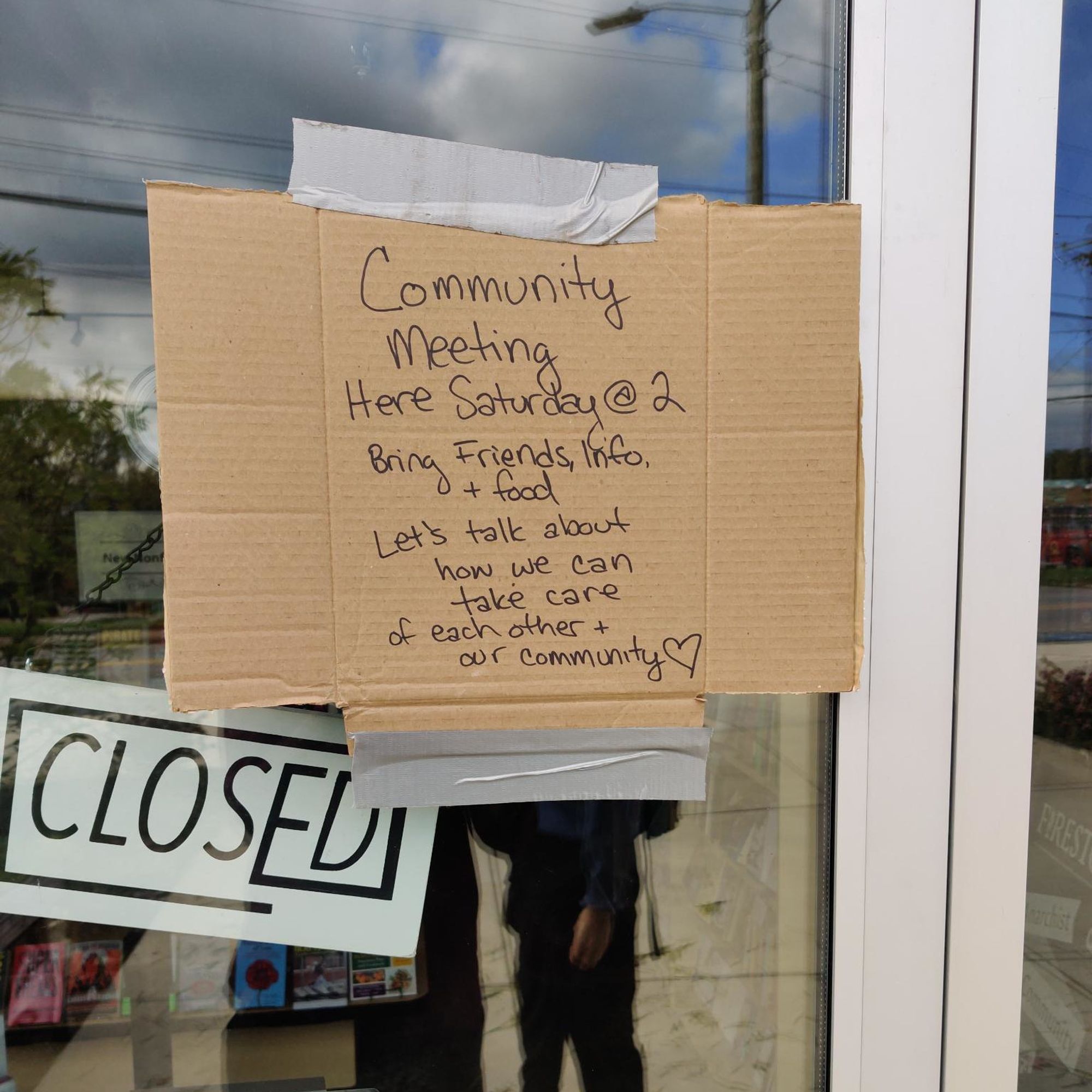 A photo of a cardboard sign taped to the closed door of Firestorm Books. It reads "Community meeting here Saturday @ 2. Bring friends, info, and food. Let's talk about how we can take care of each other and our community."