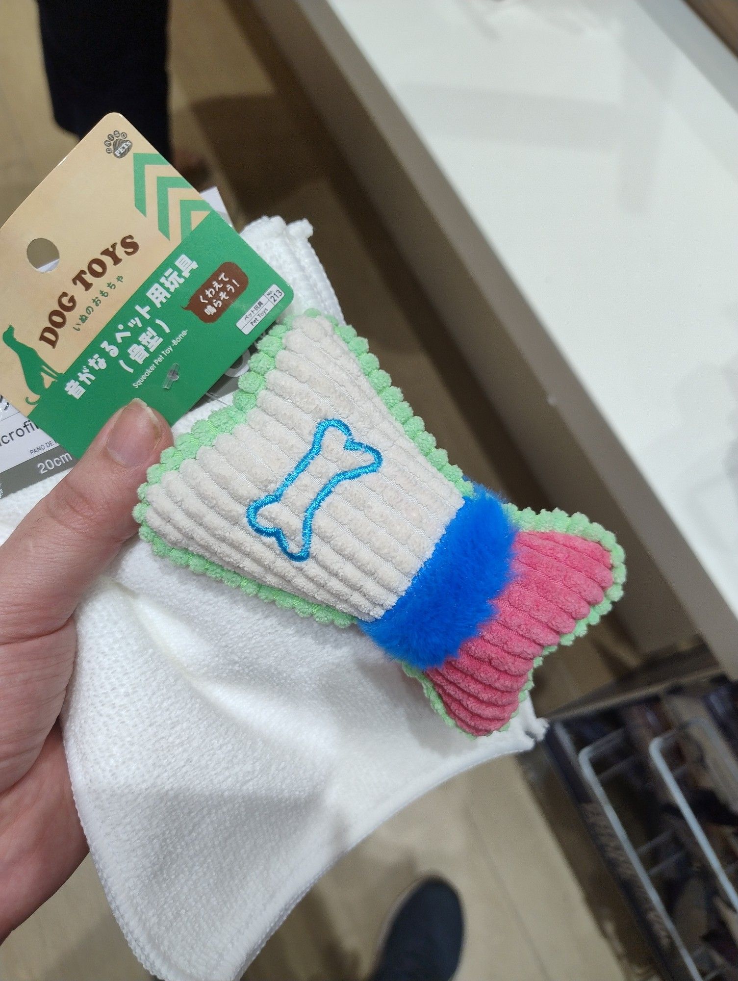 a photo of a dog toy vaguely shaped like a bone with an embroidery of a bone. It's white, blue and pink, the colors of the trans flag, with a green border but we're ignoring that part for the sake of the joke