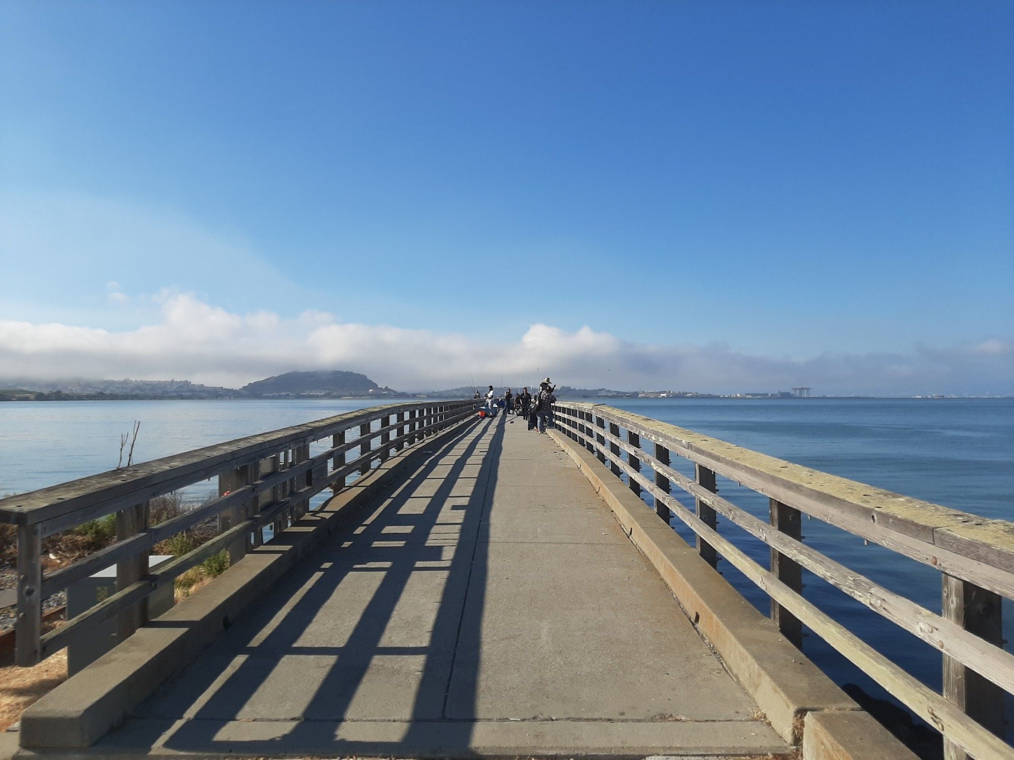 Fishers on a pier, with the San Francisco skyline hidden in a wall of clouds.