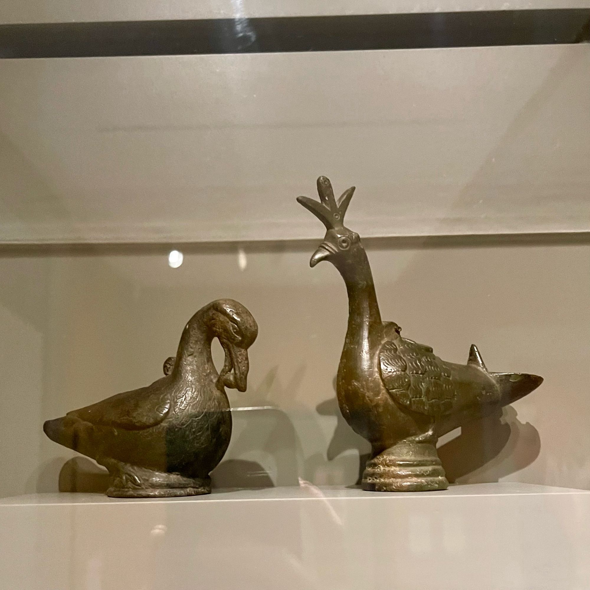 Left: bronze duck-shaped lamp, head tilted down 
Right: bronze peacock-shaped lamp